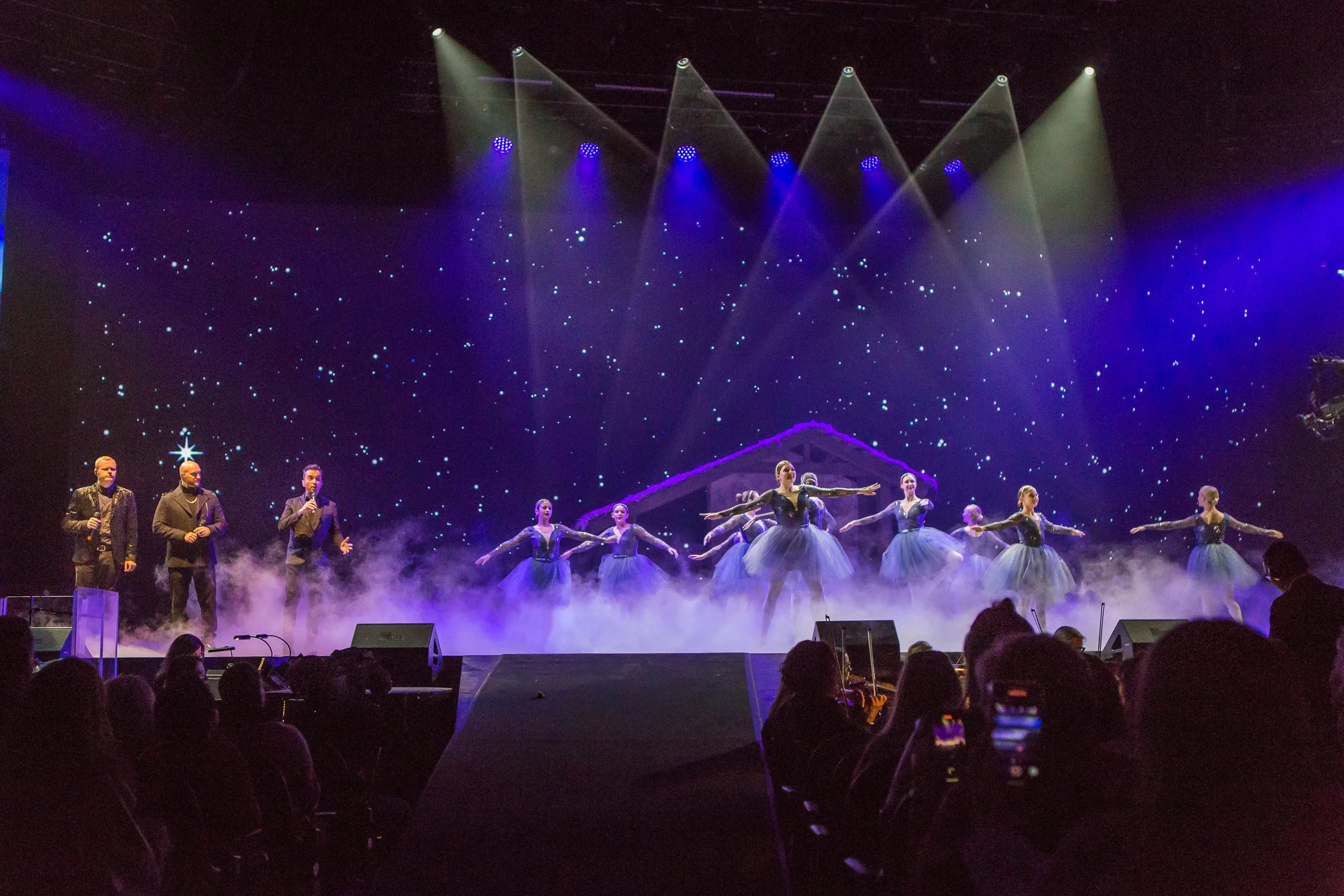 Ballet dancers performing on stage with STAR of Bethlehem, some singers, and a nativity background as part of a holiday show.