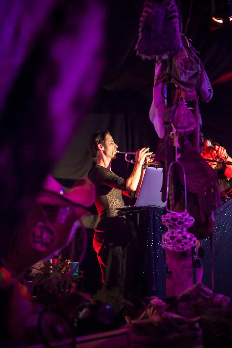 A man playing a trumpet during a performance, surrounded by colorful decorations and purple lighting.