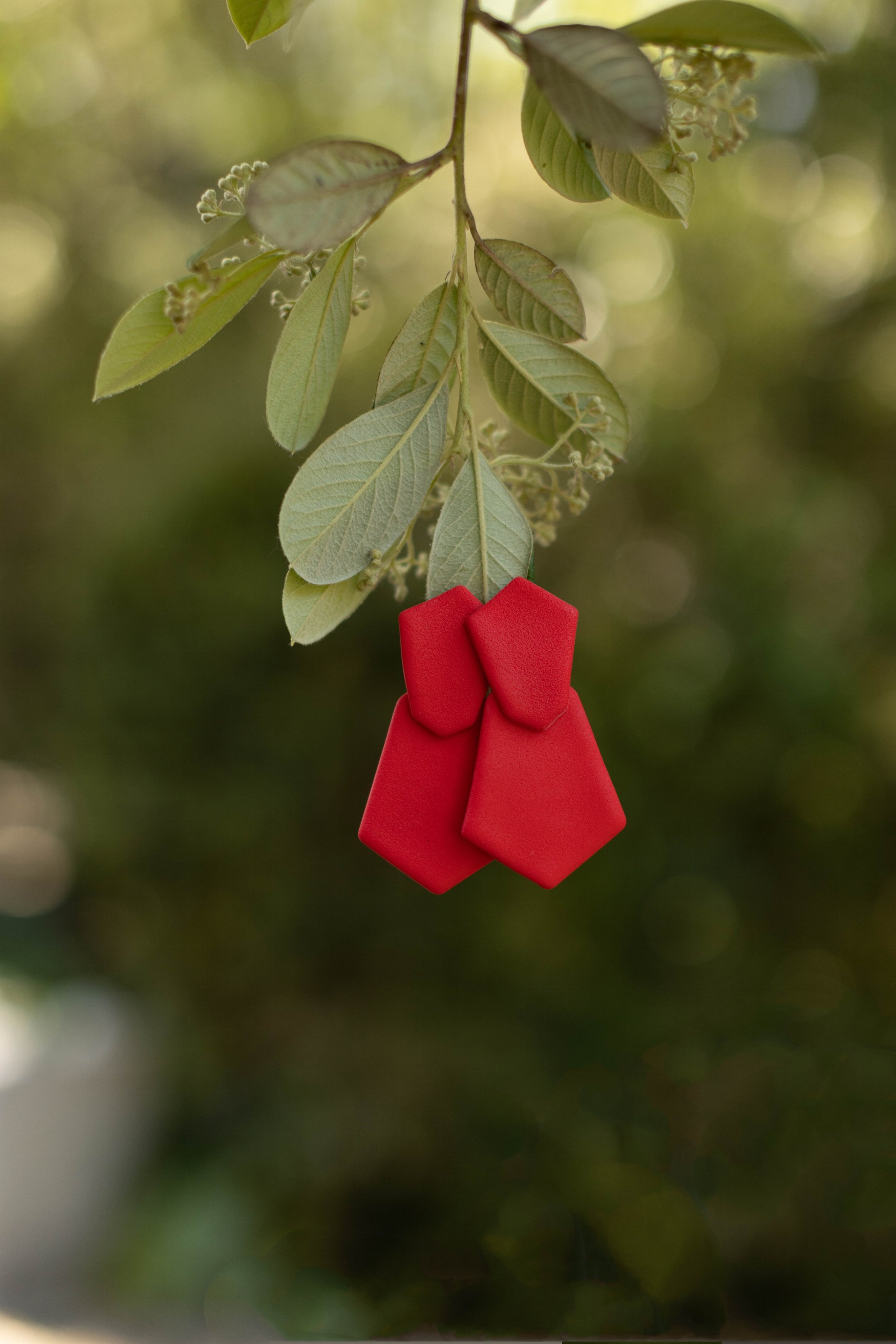 A branch with green leaves hanging down, with four red fencing corner post caps attached to the leaves.