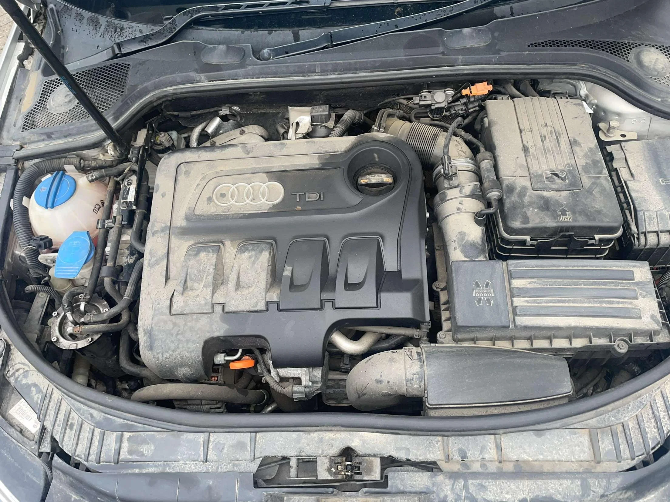View of a dust-covered Audi TDI engine in a car's engine bay.