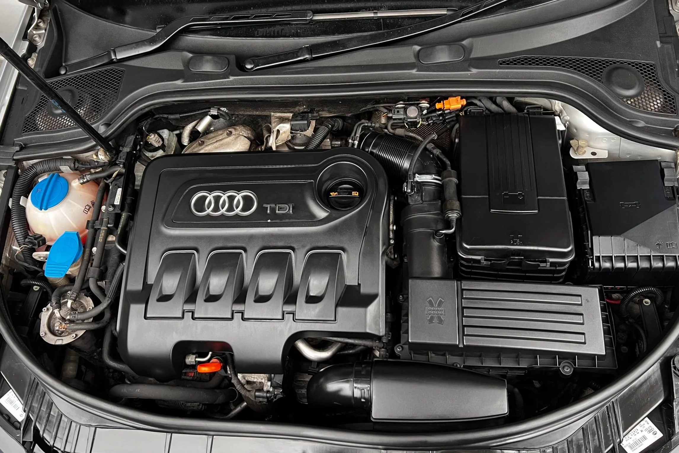 Car engine bay featuring Audi TDI engine with visible components like coolant reservoir and air intake system.