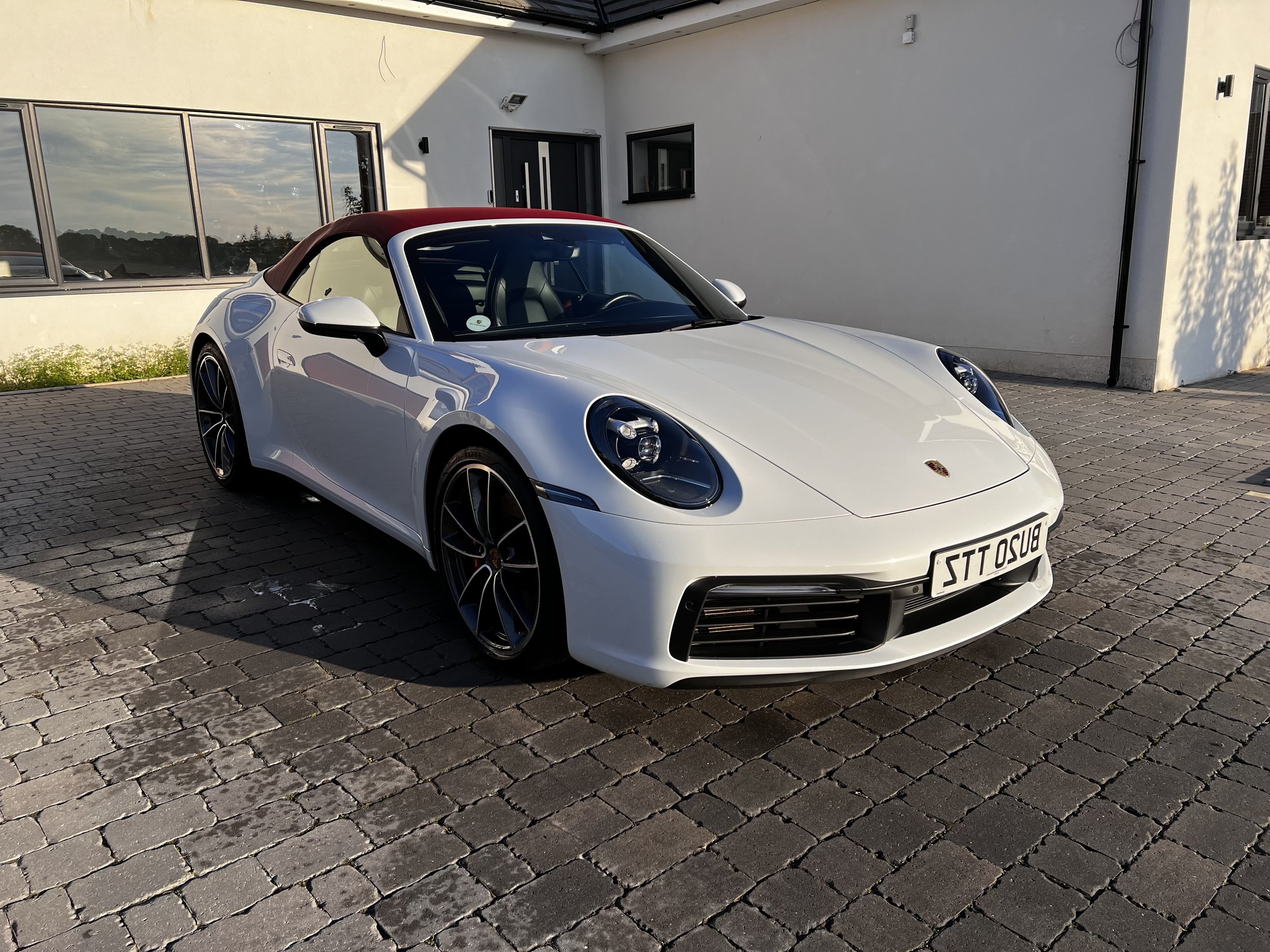 White Porsche 911 convertible with red soft top parked on stone driveway.
