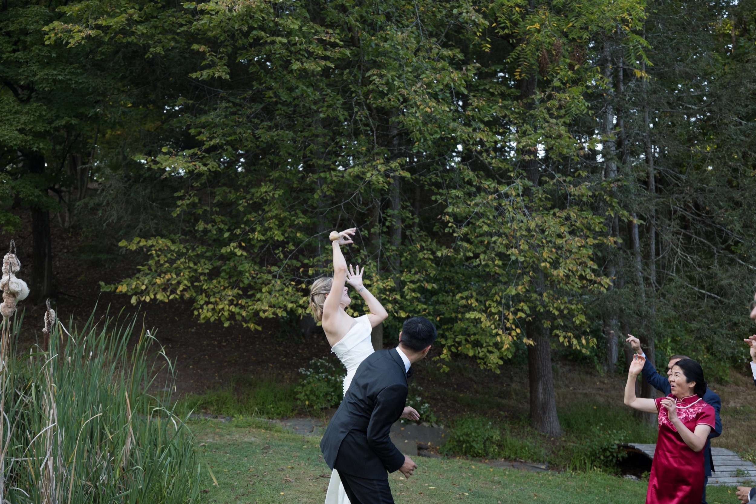 A woman in a white dress dancing outdoors among a group, with trees and greenery in the background.