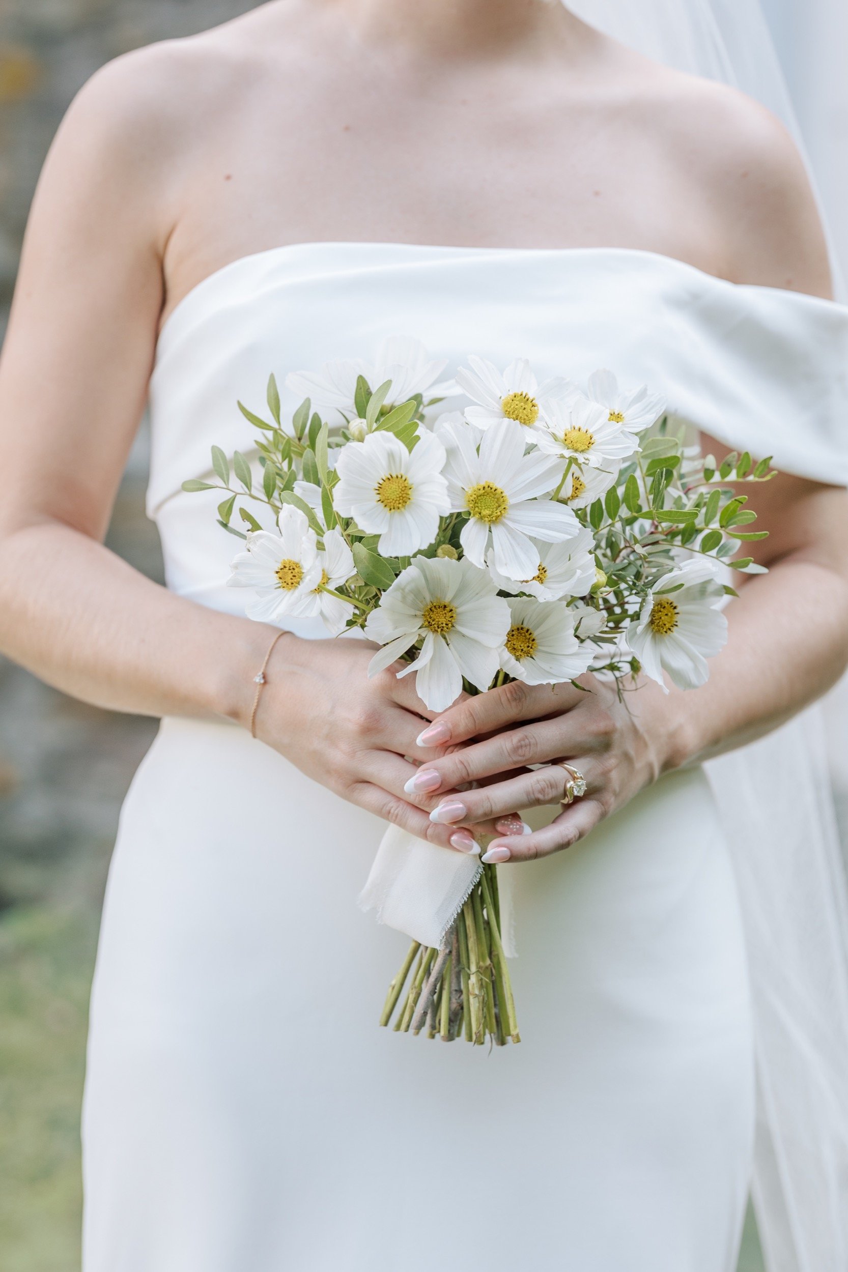 A bride holding a bouquet of white daisies and green leaves