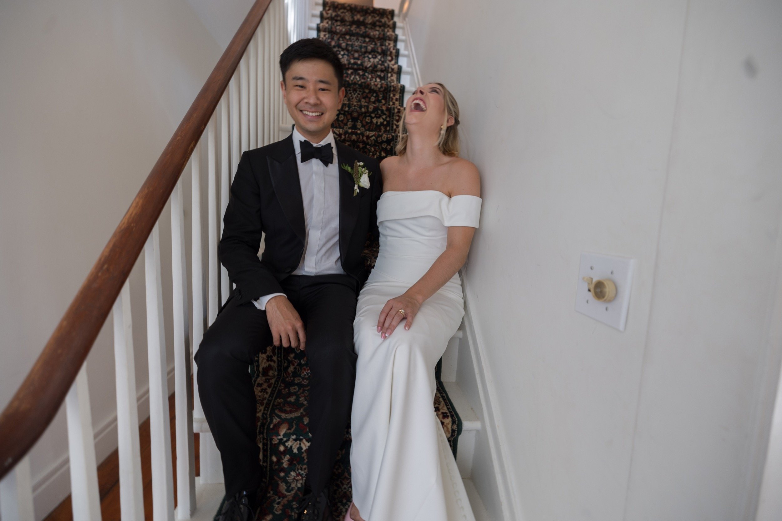 A bride and groom sitting on stairs, smiling and laughing, after their wedding ceremony.