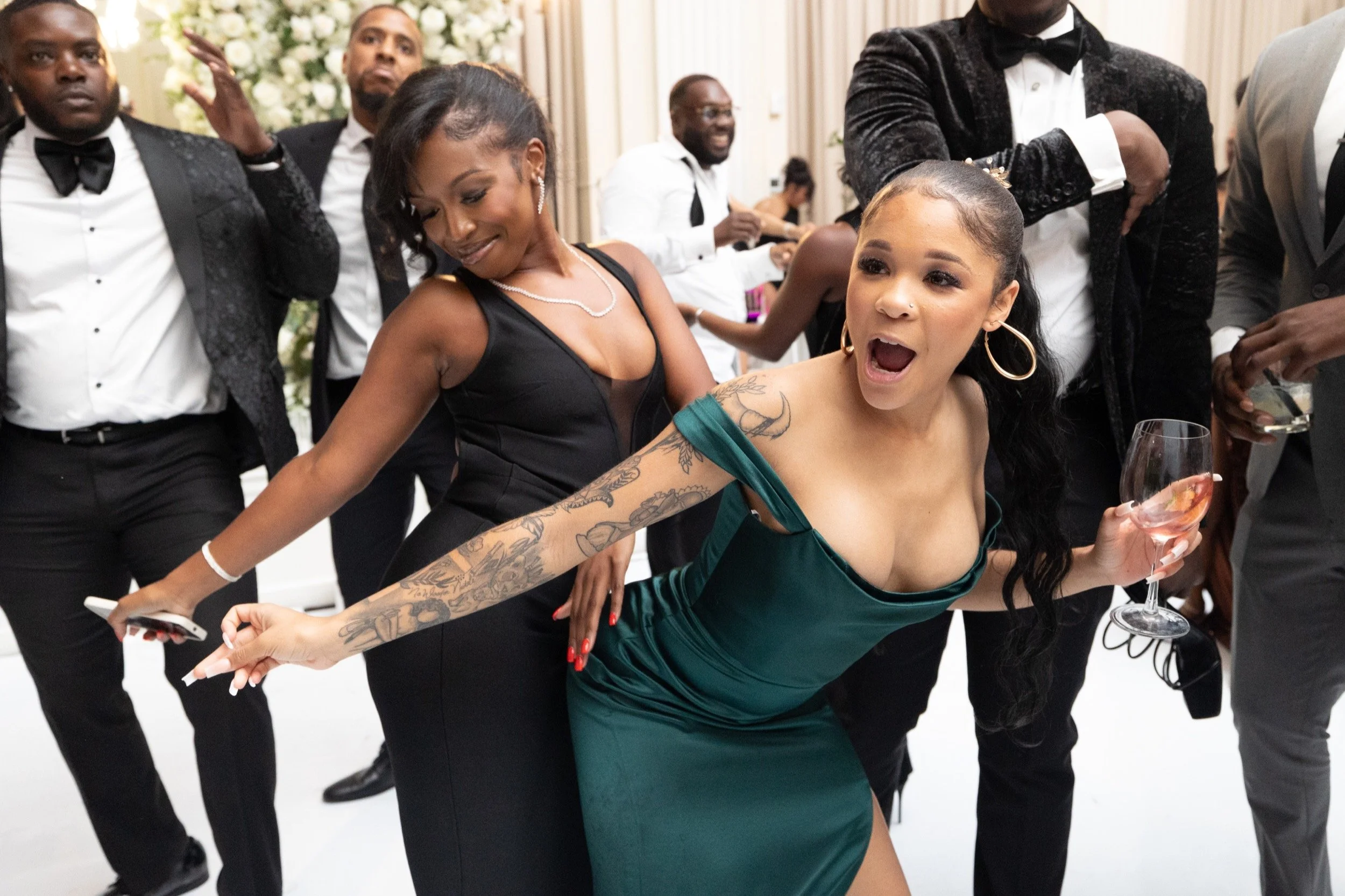 Two friends laugh and dance on the dance floor at a Black tie wedding reception.