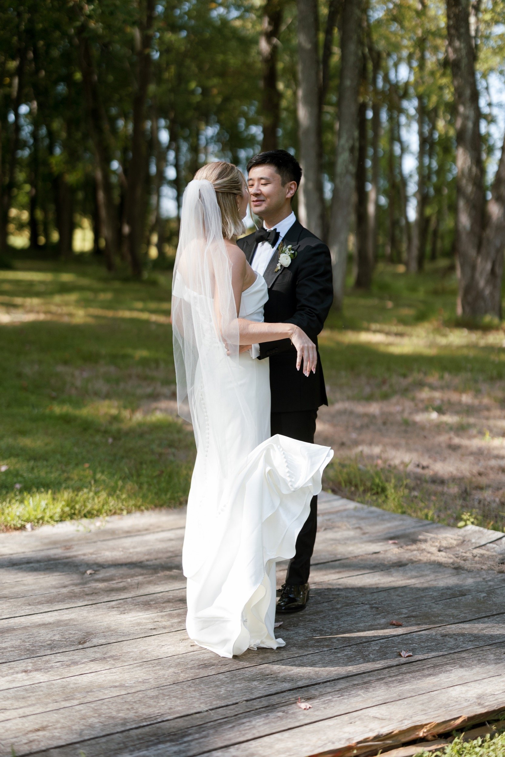 A bride and groom sharing a dance outdoors on a wooden platform surrounded by trees