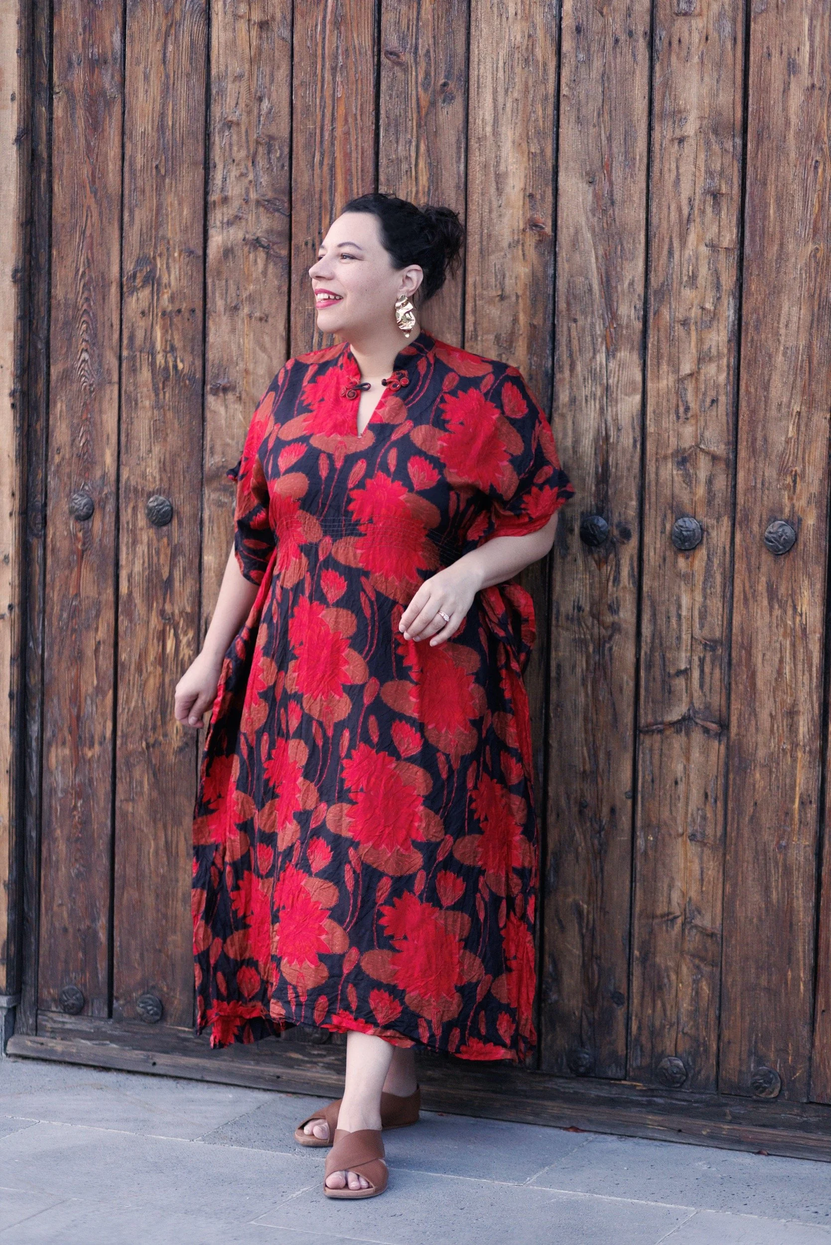 Amber Marlow in a vintage red kimono, standing on a wooden door in Mexico. She is wearing large gold earrings and brown leather sandals.