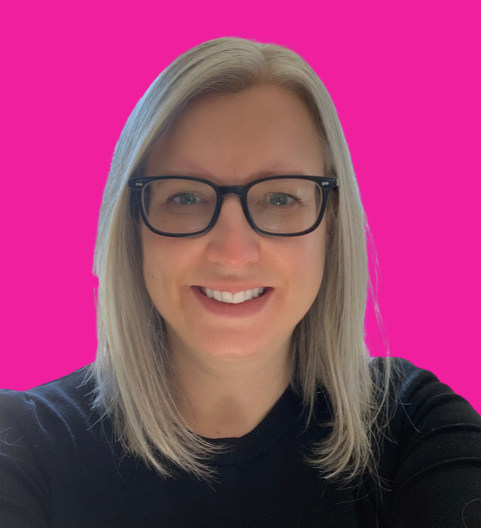 A woman with light blonde hair, glasses, and a black shirt smiling in front of a bright pink background.