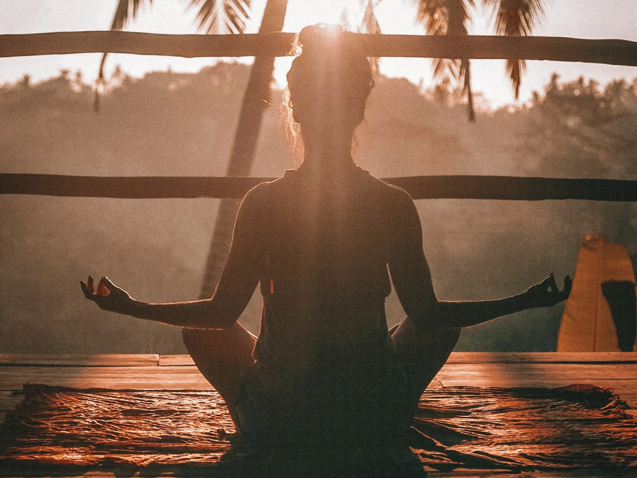 Silhouette of a person practicing yoga in a cross-legged seated meditation pose outdoors during sunset.