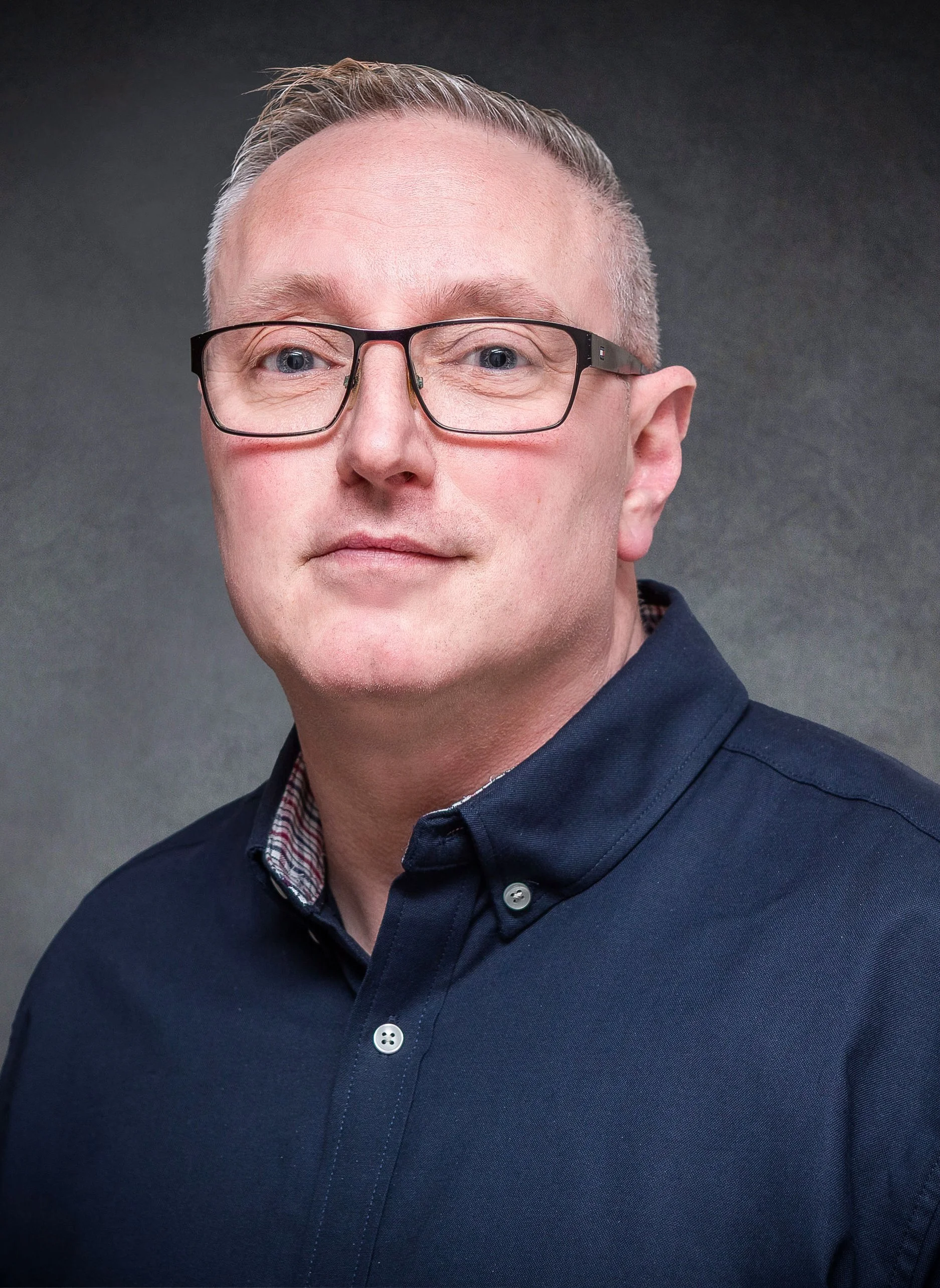 Portrait of a man wearing glasses and a dark shirt against a gray background.