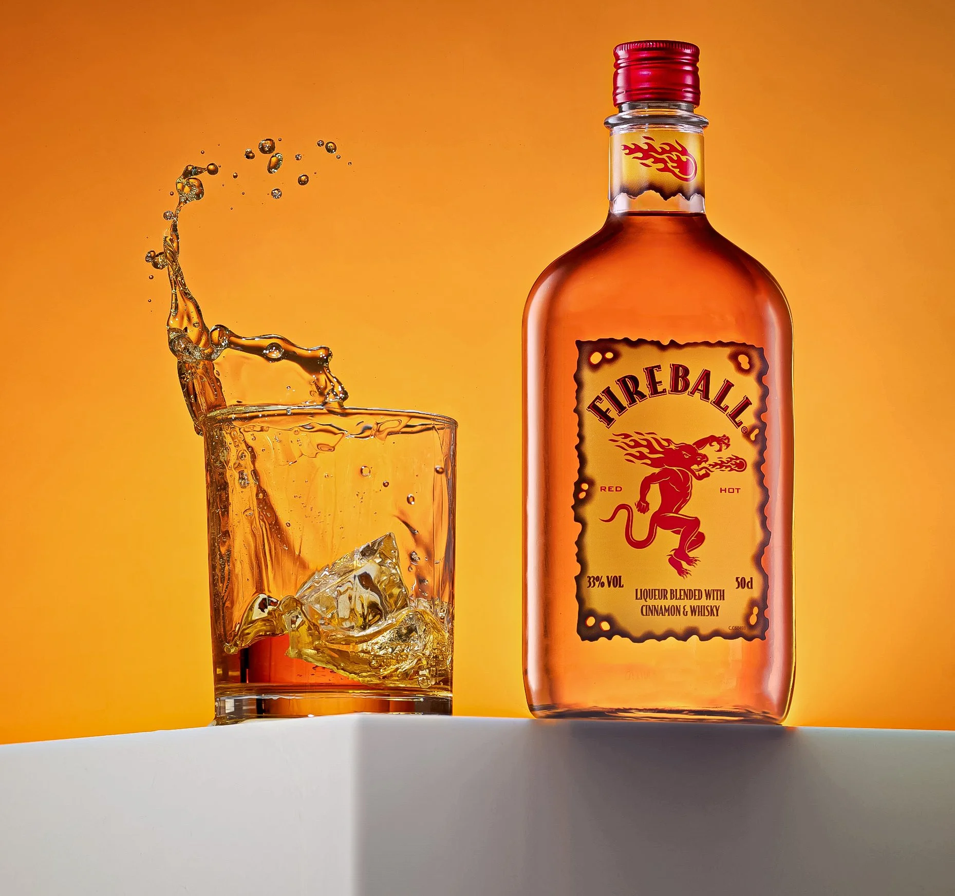 A bottle of Fireball Cinnamon Whisky next to a glass with ice and a splash of the whisky.