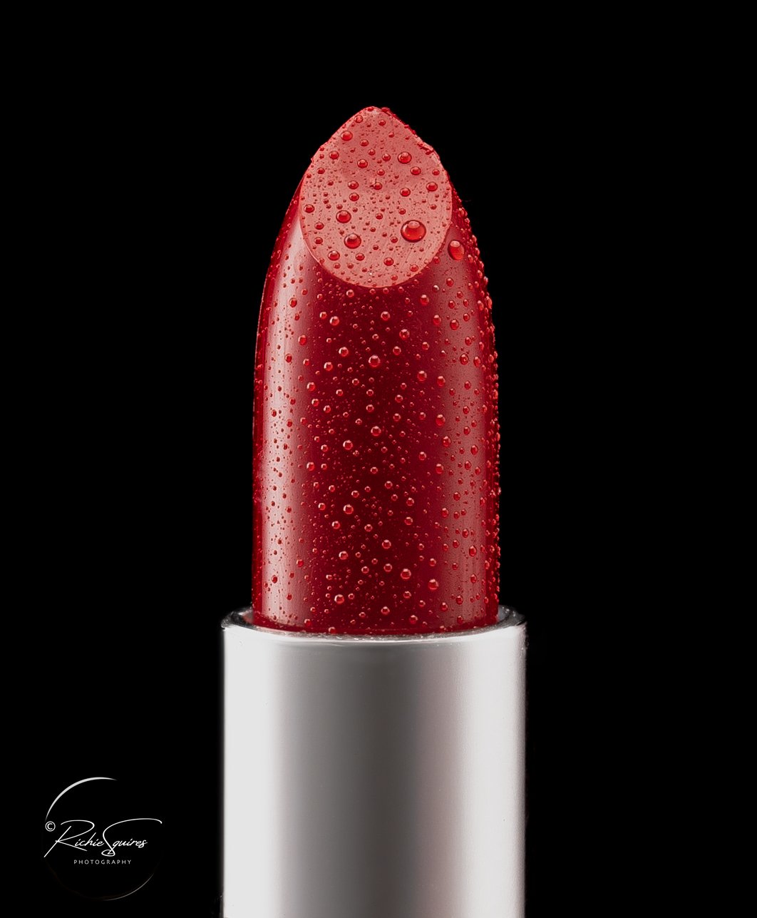Close-up of a red lipstick with water droplets on a black background.