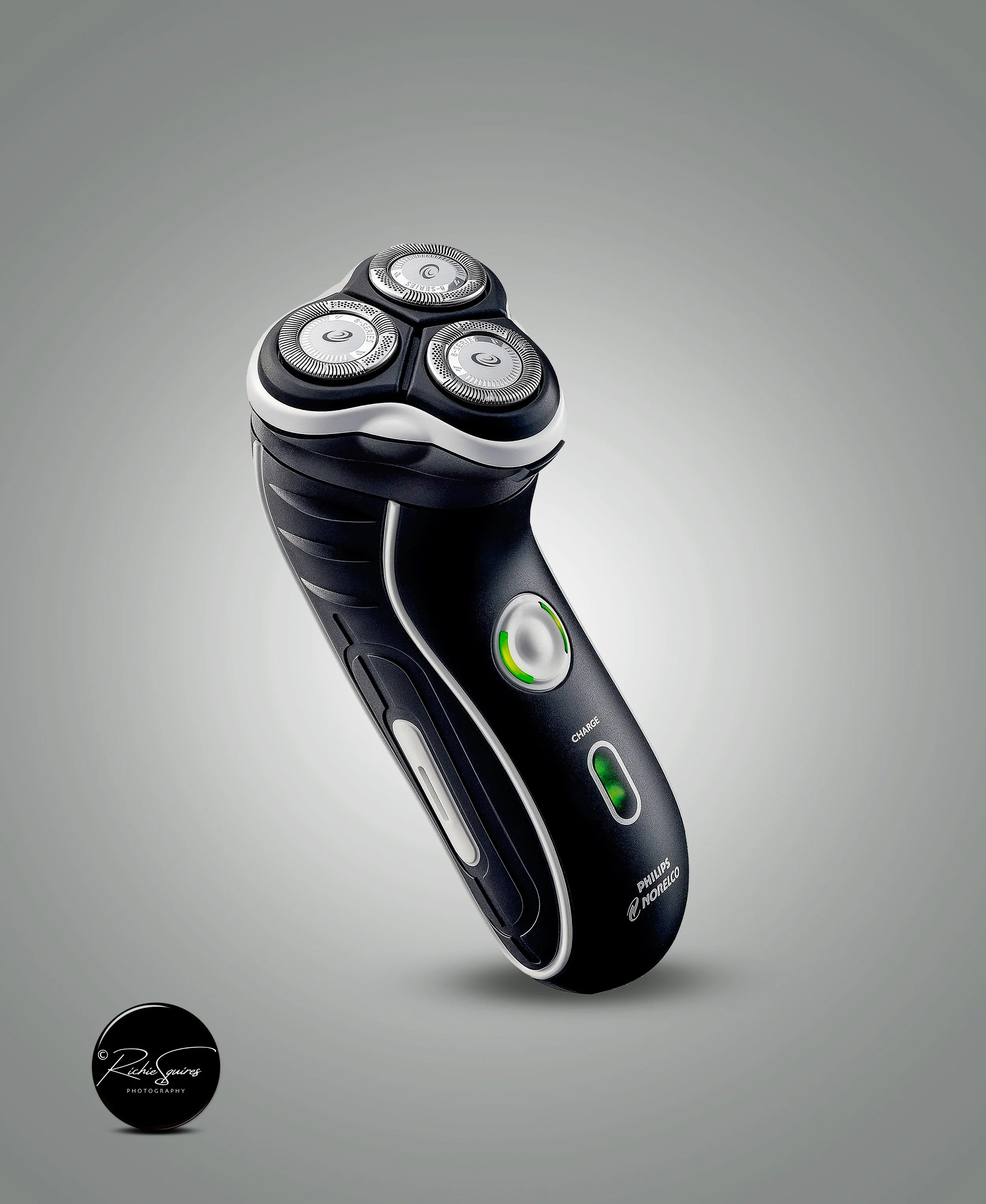 Electric rotary shaver with three circular heads, black and silver design, displayed on a gray background.