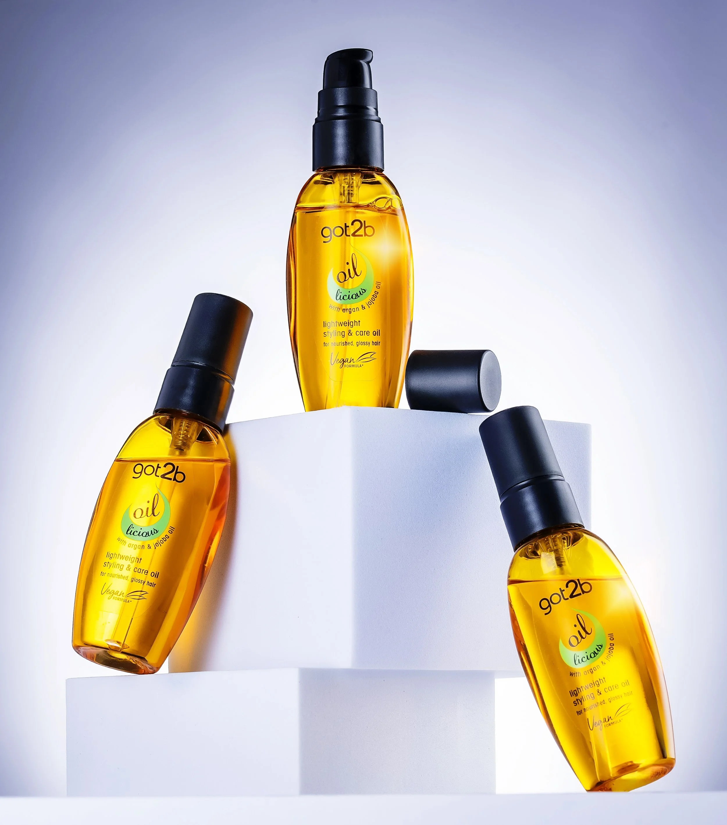 Three bottles of got2b oil-licious argan hair styling oil displayed on white blocks.