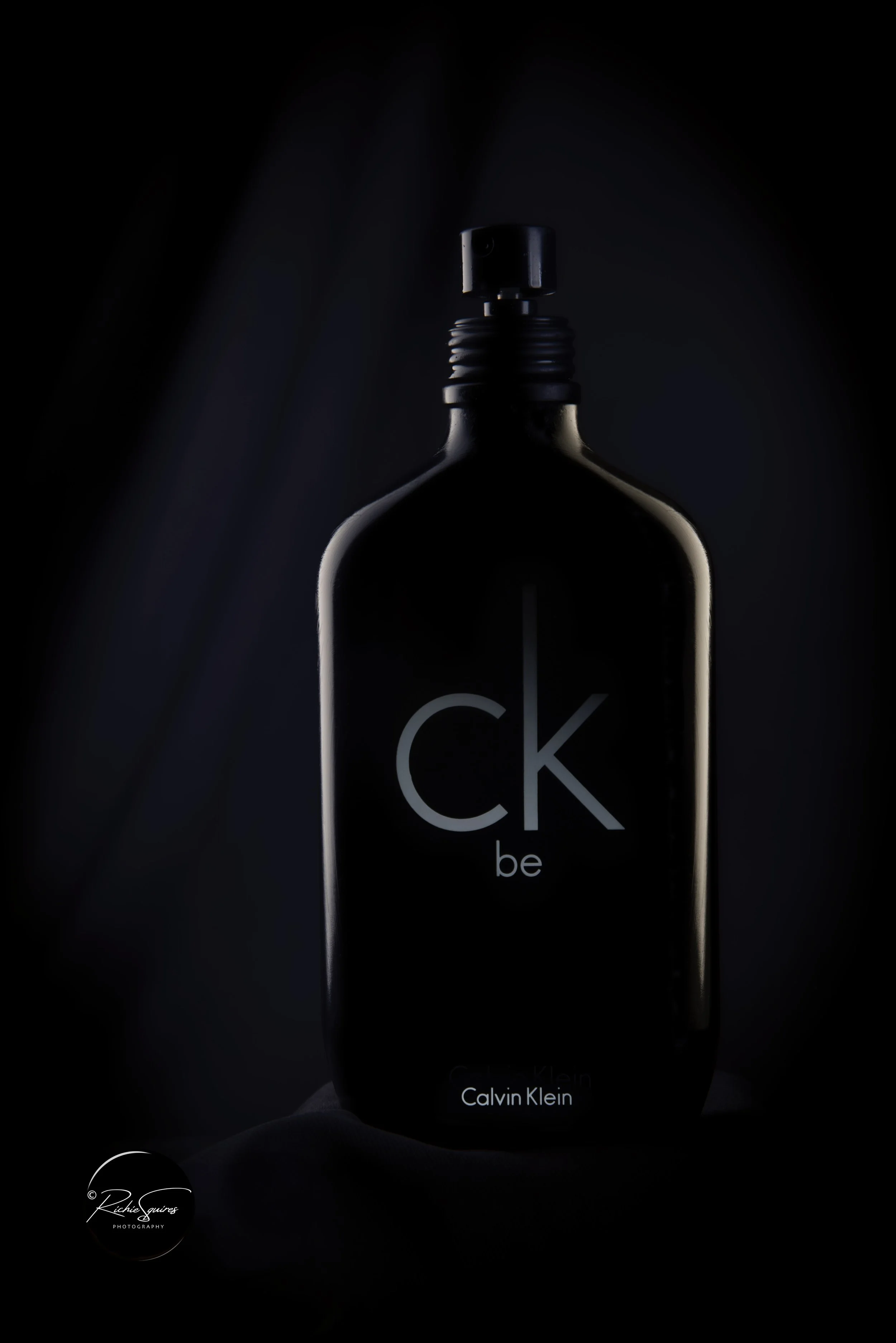 Black bottle of Calvin Klein CK Be fragrance against a dark background.