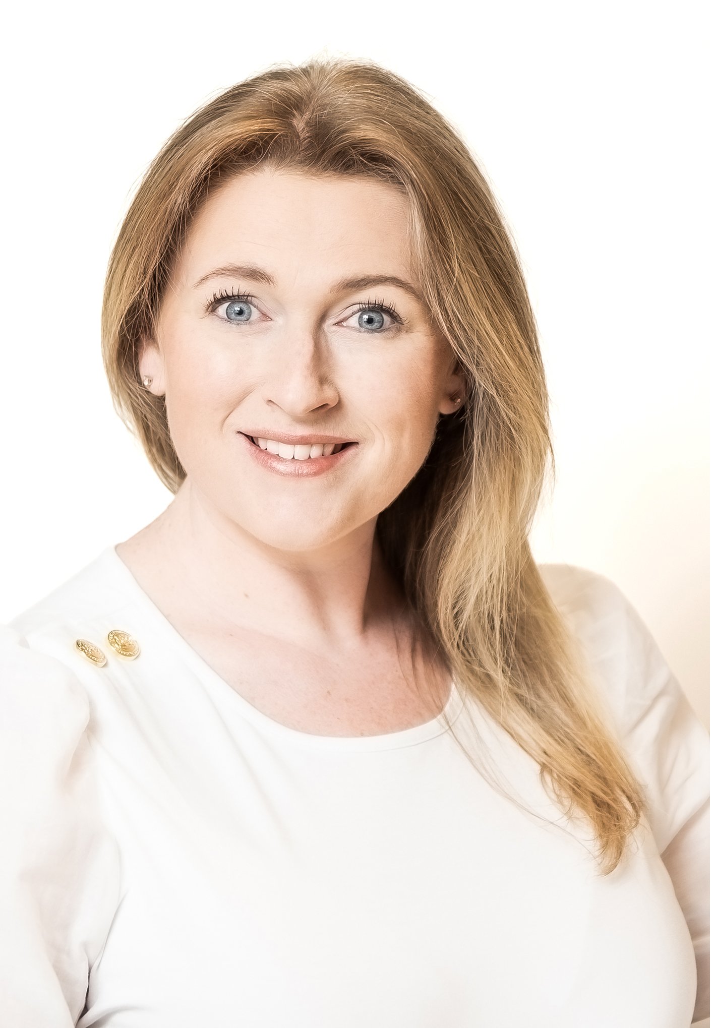 Smiling woman with long blonde hair wearing a white top against a white background.