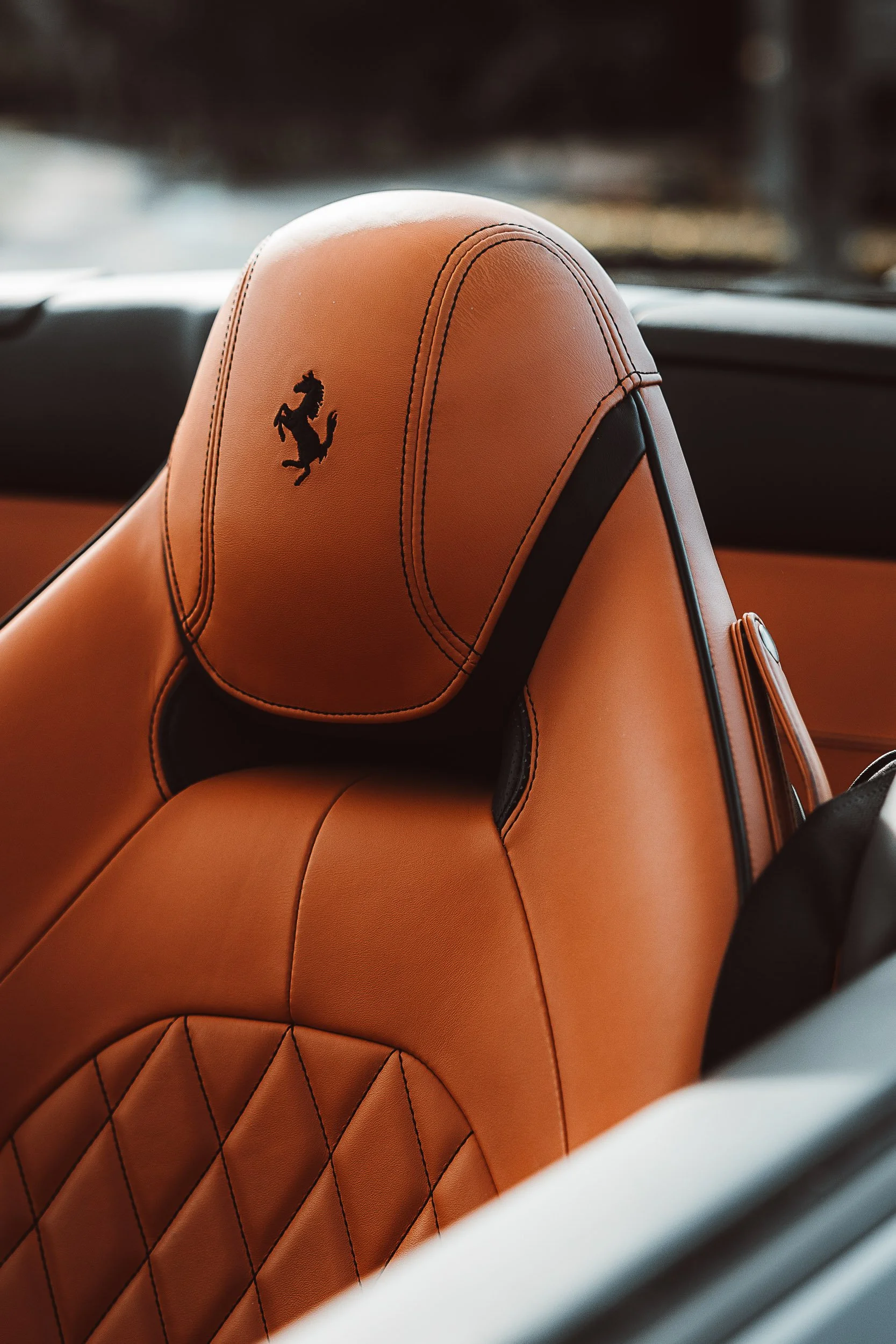 Close-up of a tan leather car seat with a prancing horse logo.
