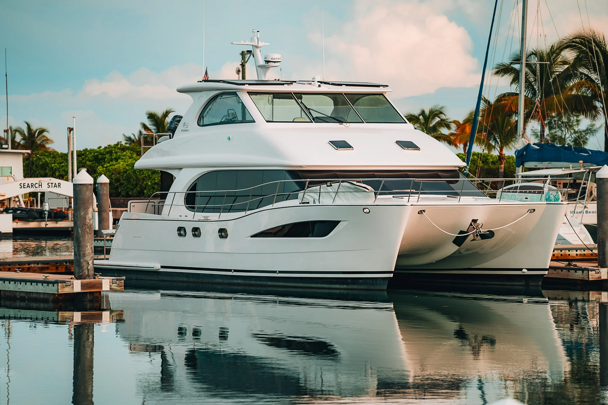 Luxury yacht docked at marina with palm trees in the background.