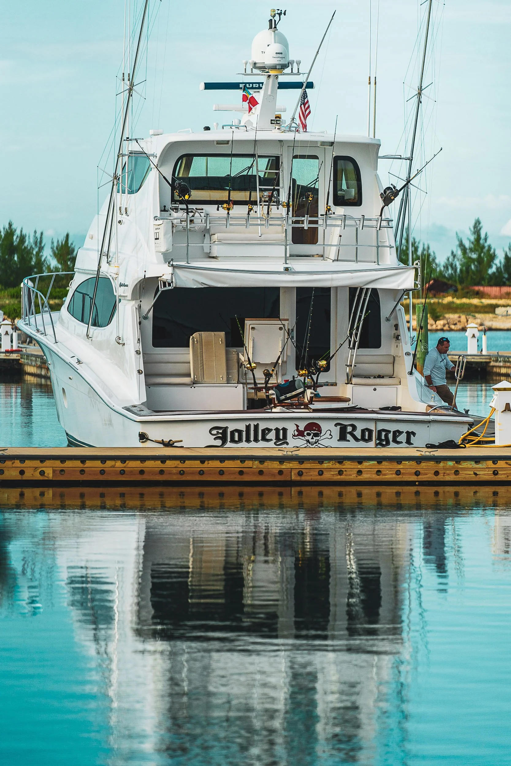 Fishing yacht named "Jolley Roger" docked at a marina, with rods and equipment visible on the deck.