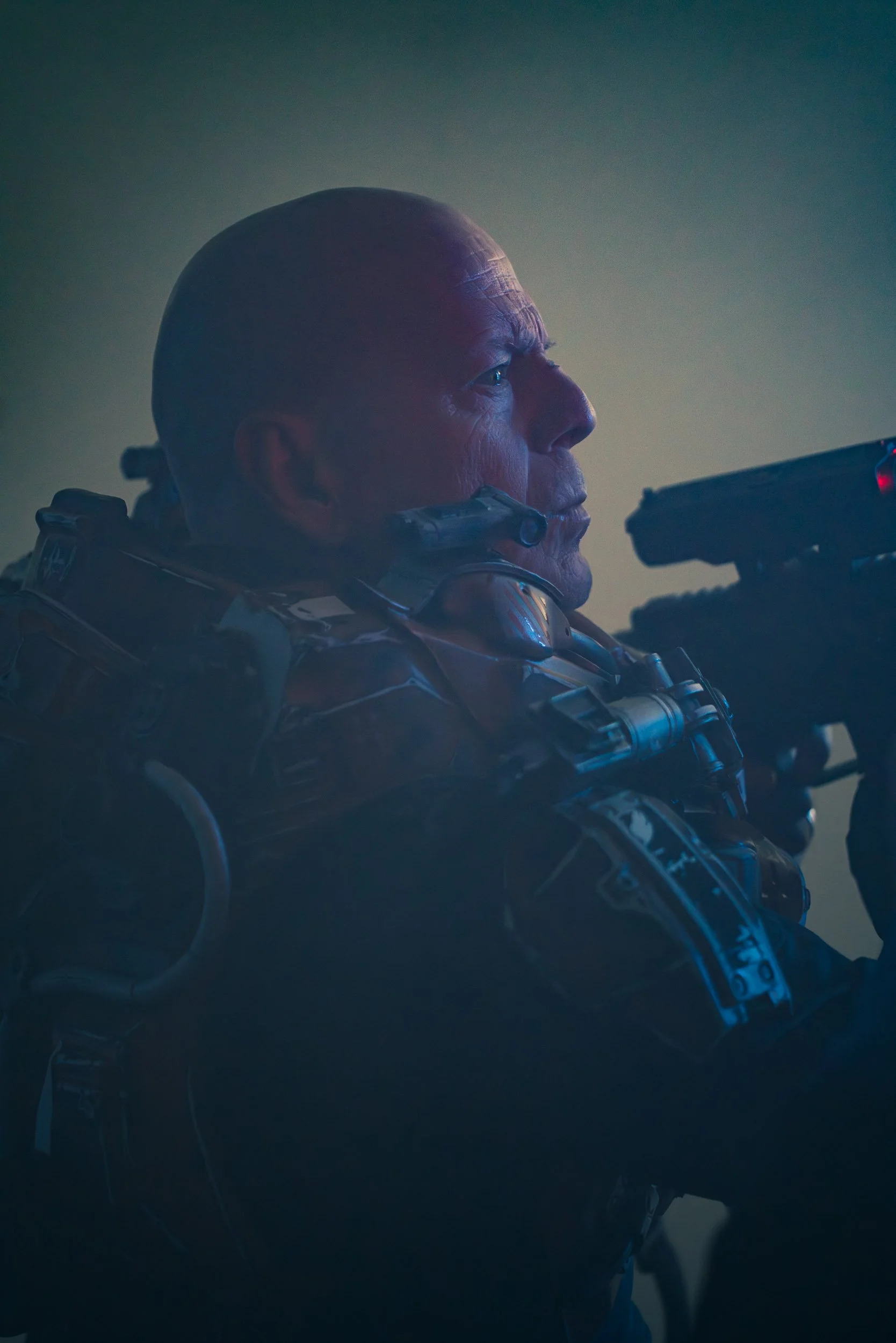 Person in armor aiming a futuristic weapon in a dimly lit setting.