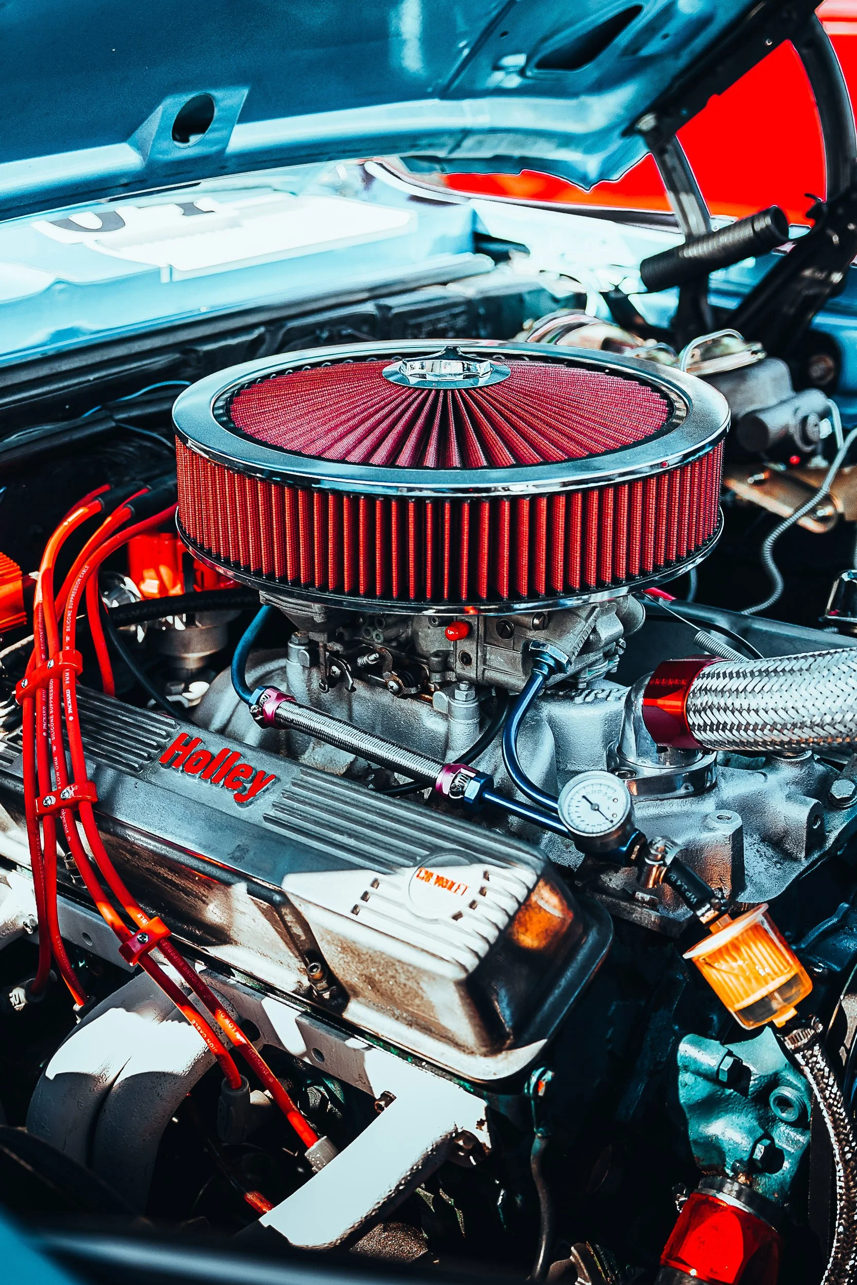 High-performance car engine with red air filter and Holley valve covers, featuring various hoses and components under an open hood.