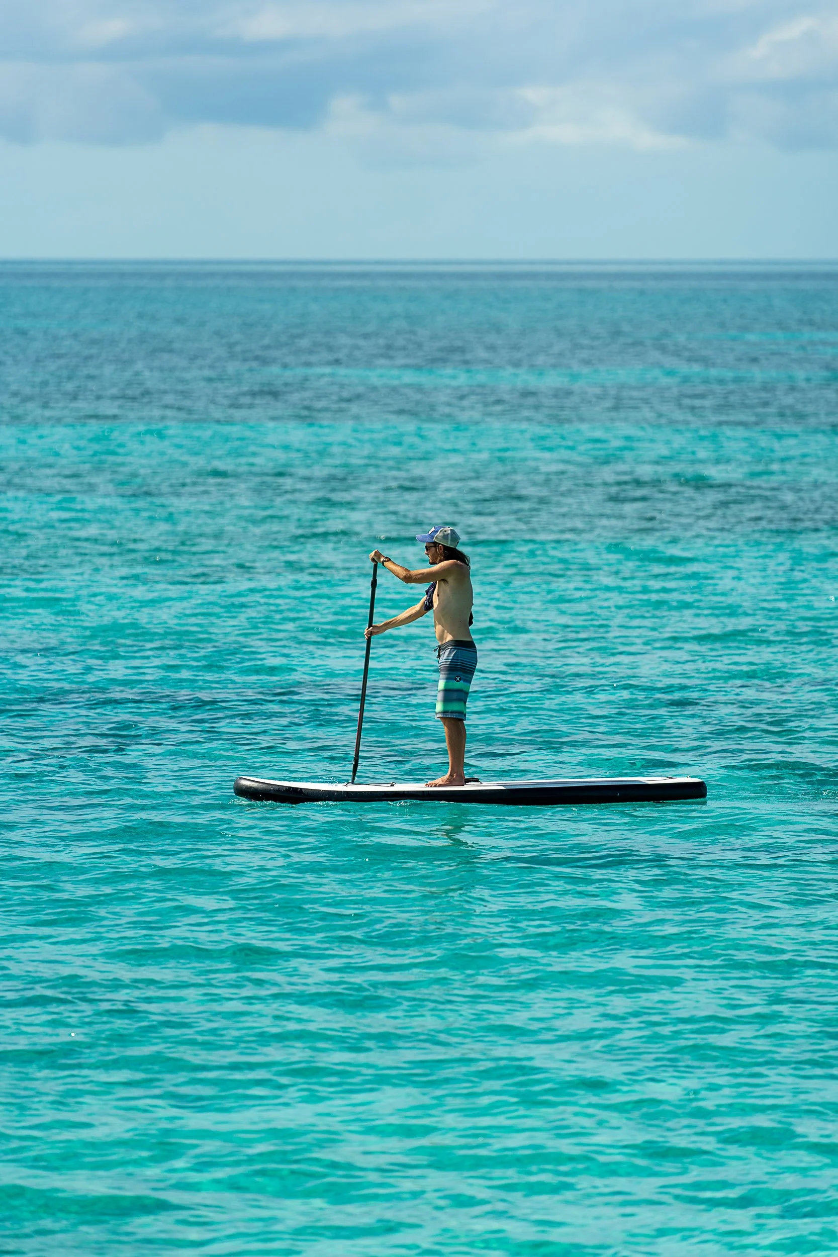 Person paddleboarding on calm turquoise water under a cloudy sky.