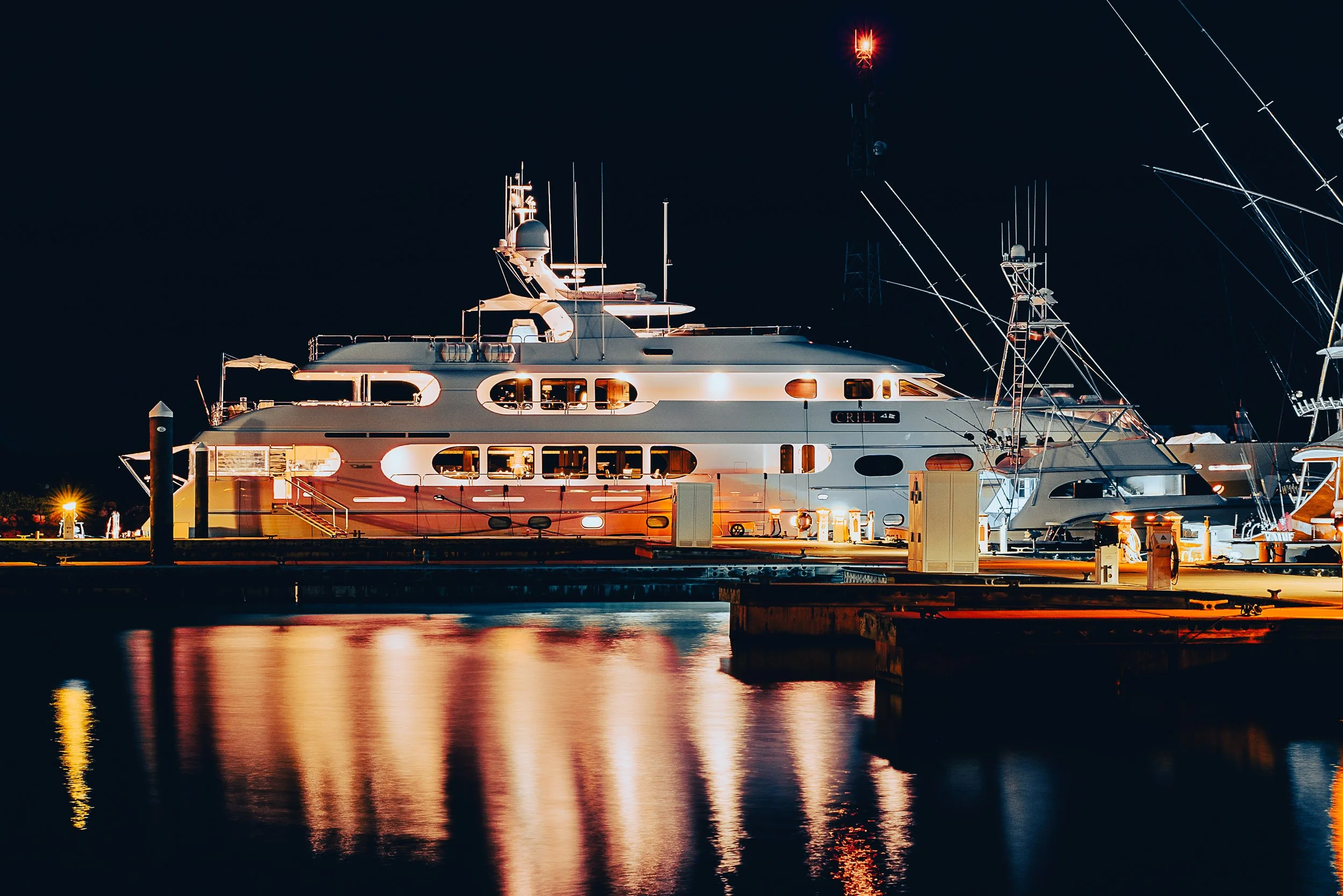 Luxury yacht docked at marina at night with reflections on water.