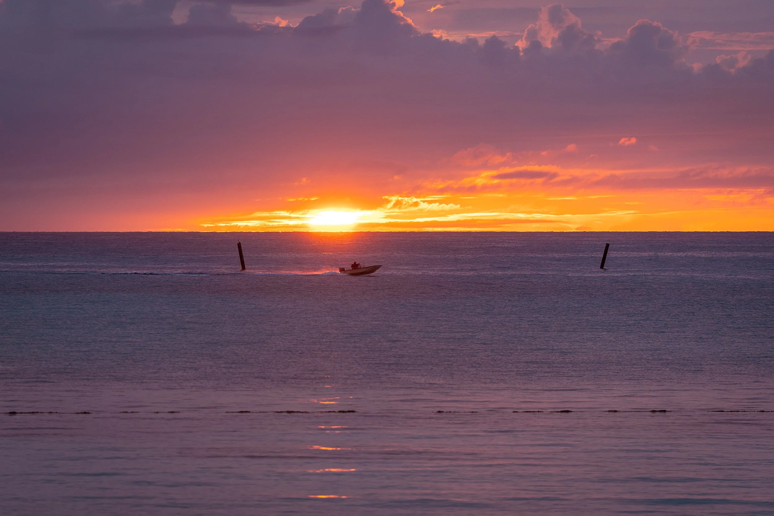 Boat on ocean during sunset with vibrant orange and purple sky.