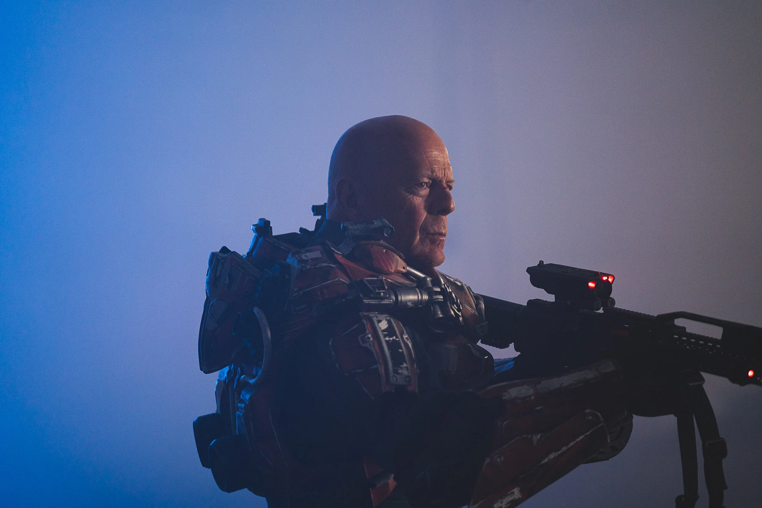Person in futuristic armor holding a weapon in a dimly lit setting.