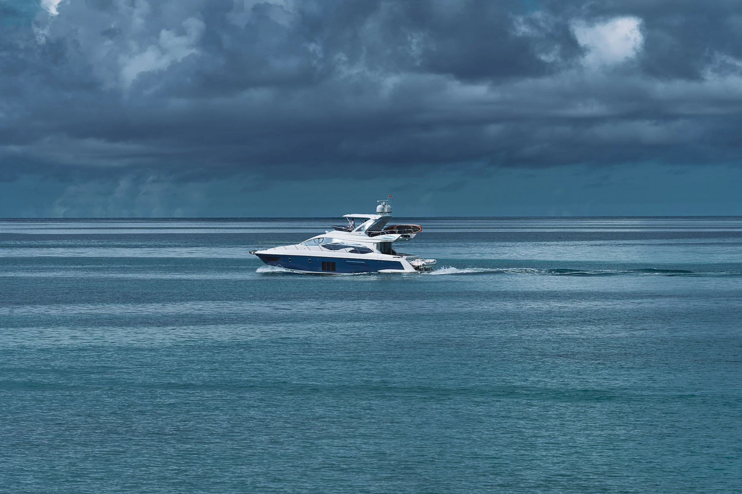 A white yacht moving on a calm ocean with storm clouds overhead.