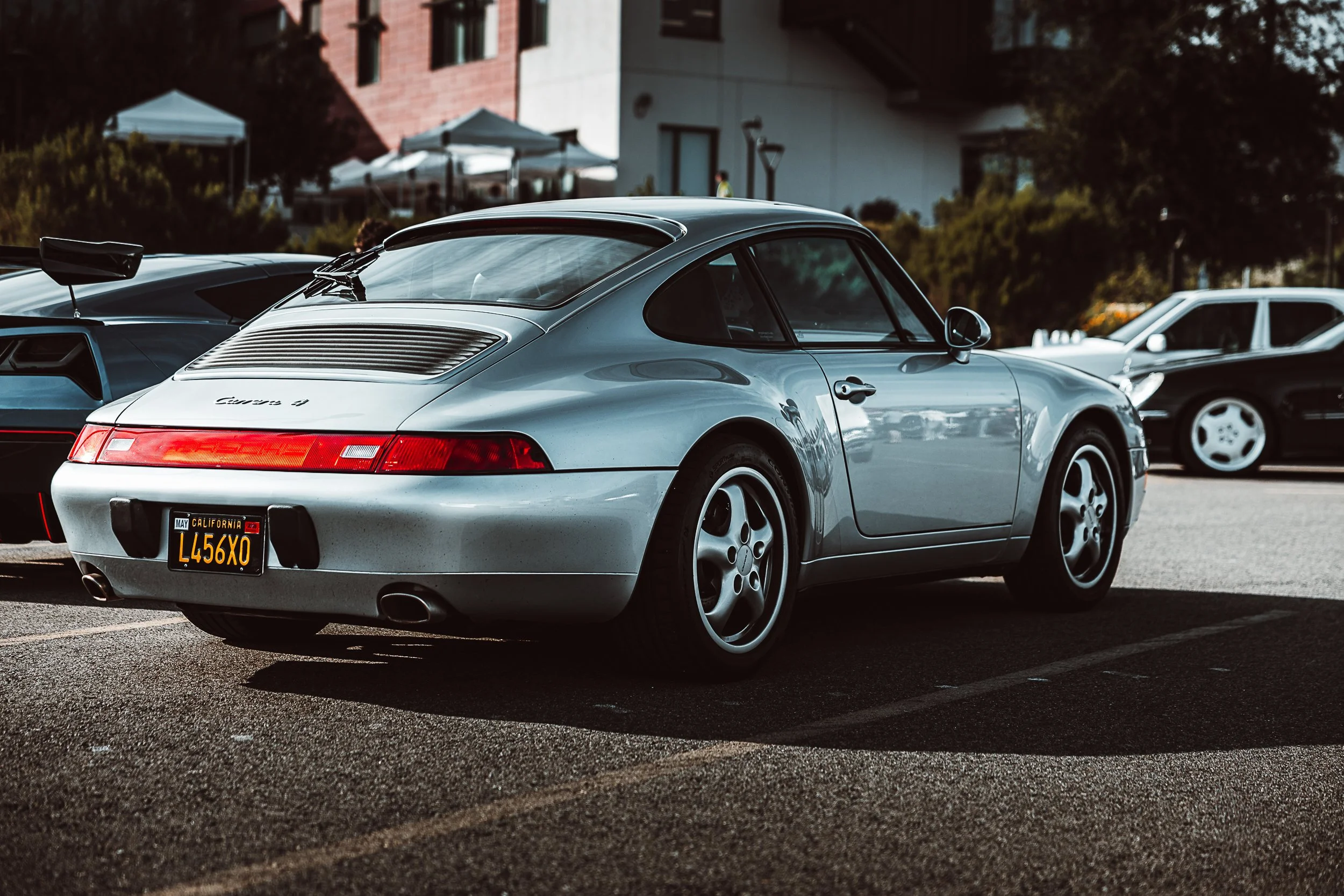 Silver Porsche 911 parked in a lot during daytime, with a California license plate L456XO, with other cars and trees in the background.