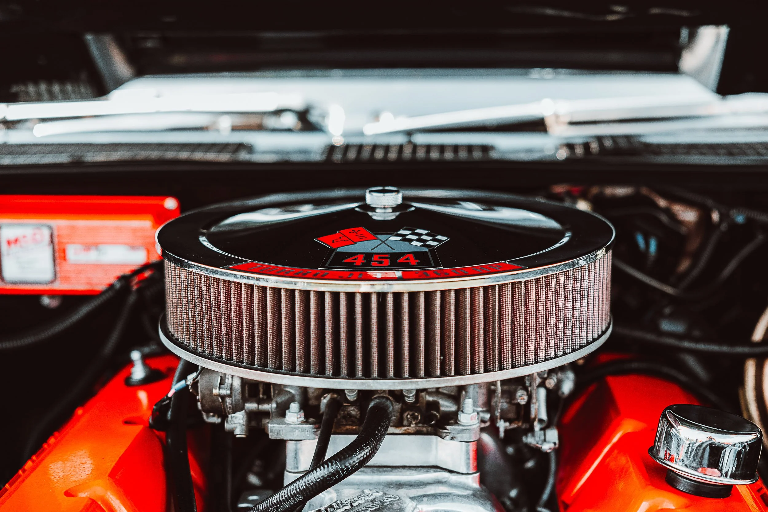 Close-up of a classic car's engine with a chrome air filter cover labeled '454 cubic inches' and a checkered flag design.