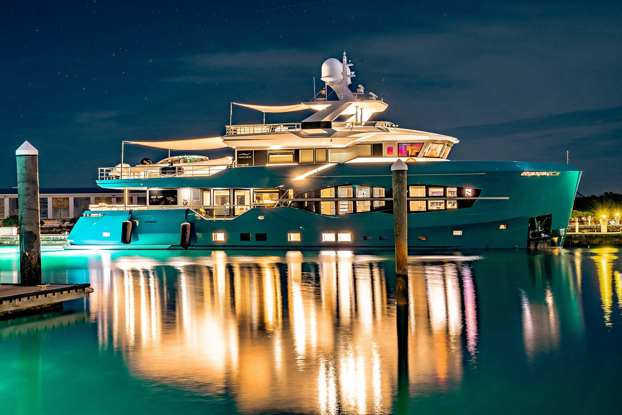 Luxurious yacht docked at night with lights reflecting on water