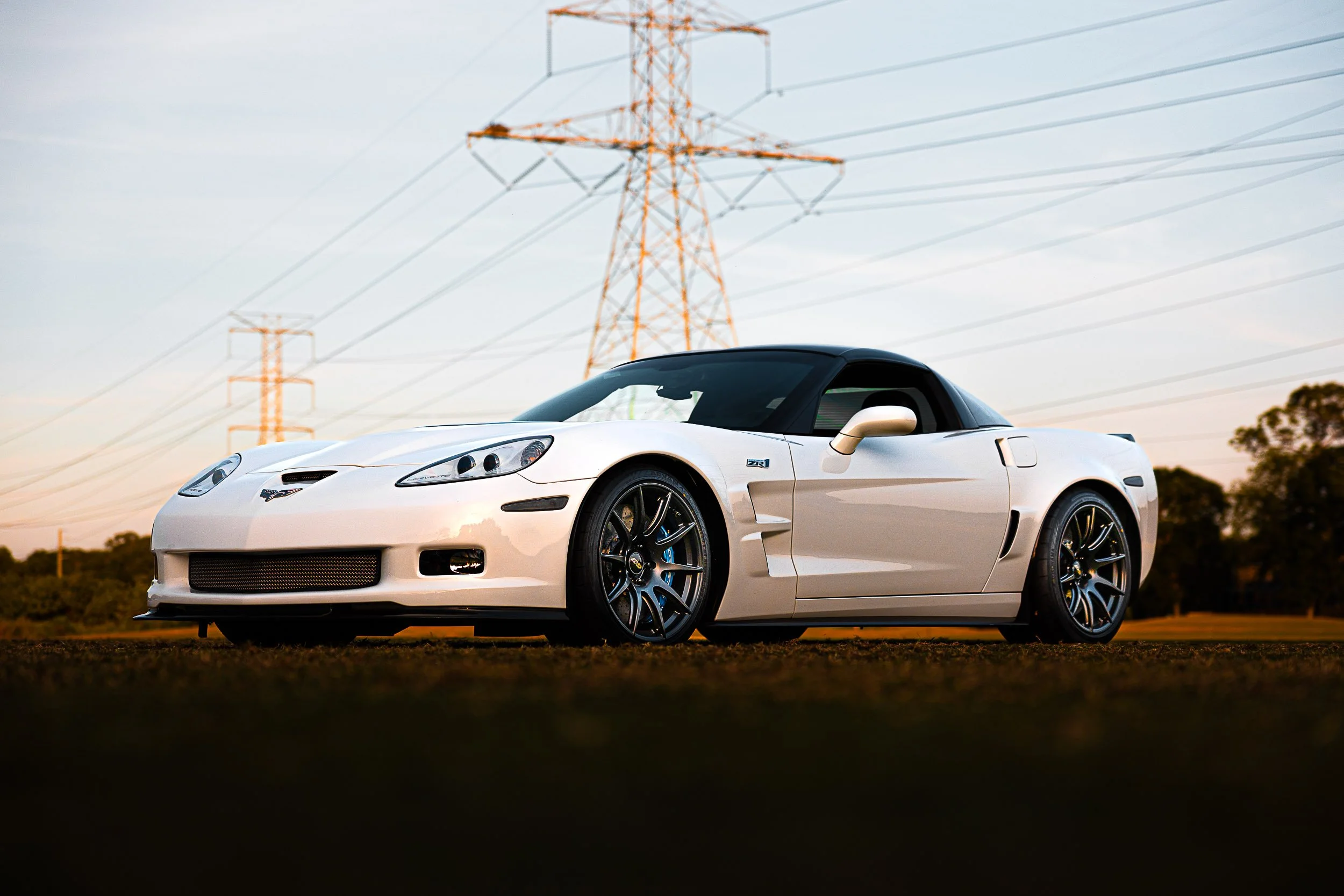 White sports car parked outdoors near electric pylons, side view.