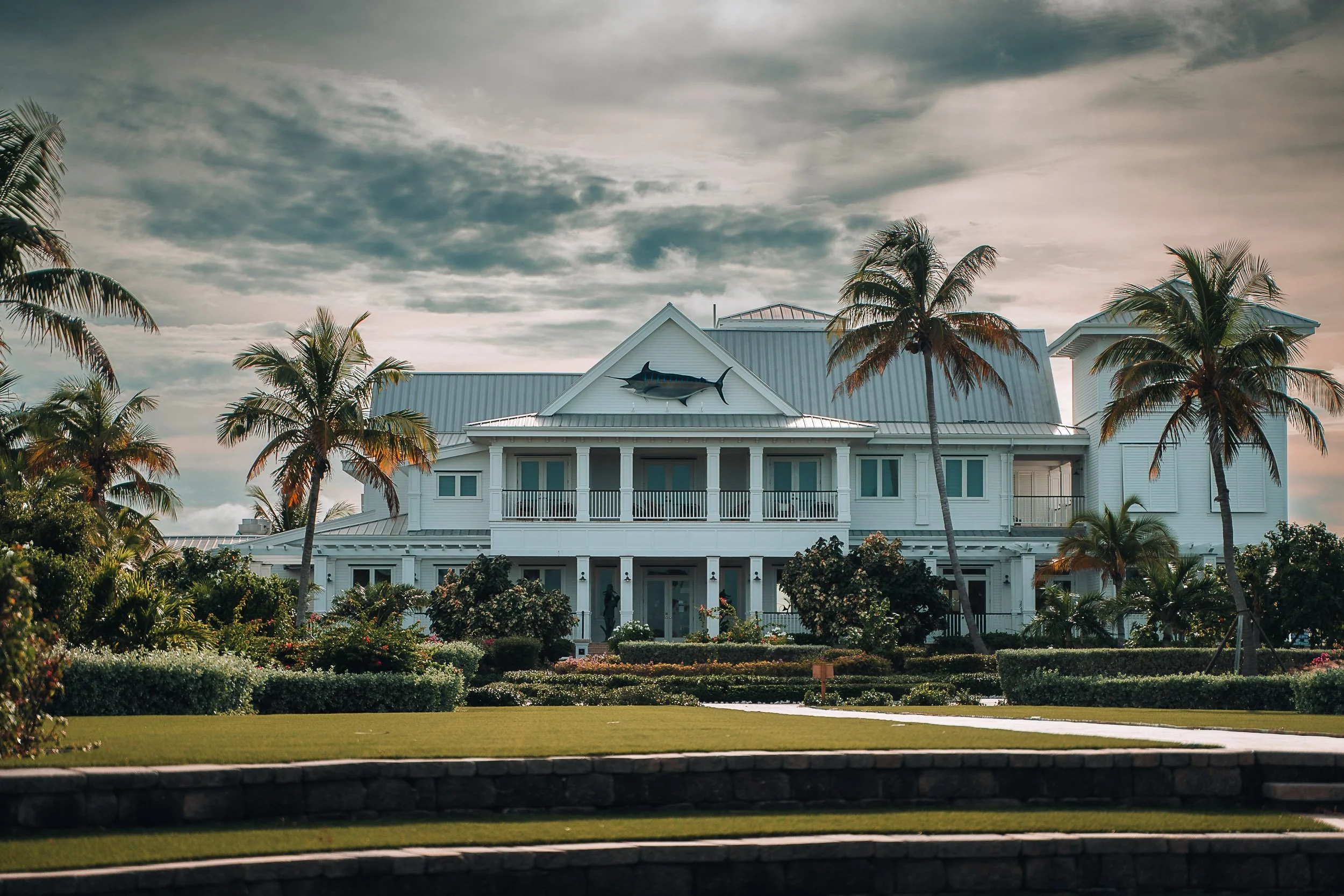 Large white coastal house with palm trees and a fish sculpture on its facade.