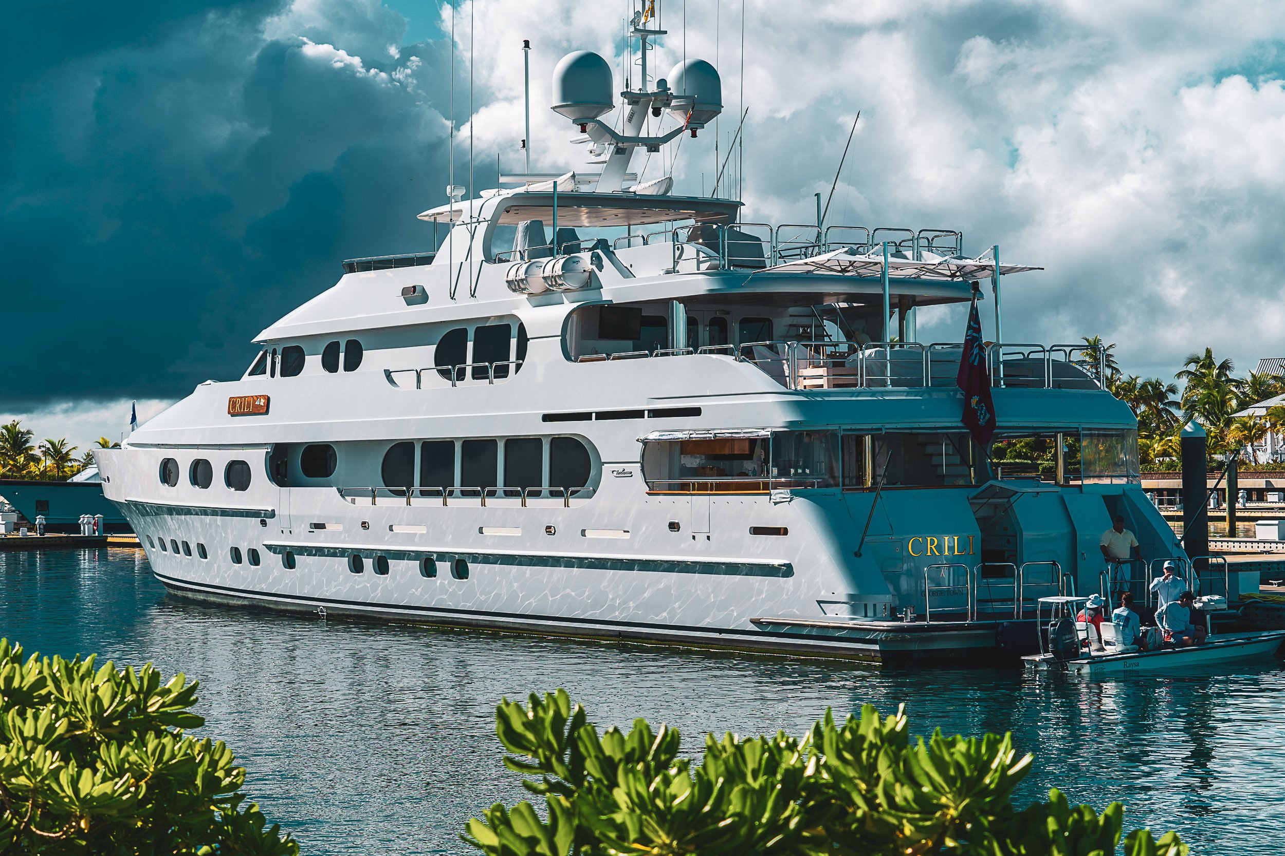 Luxury yacht docked in a marina with lush greenery and cloudy skies.
