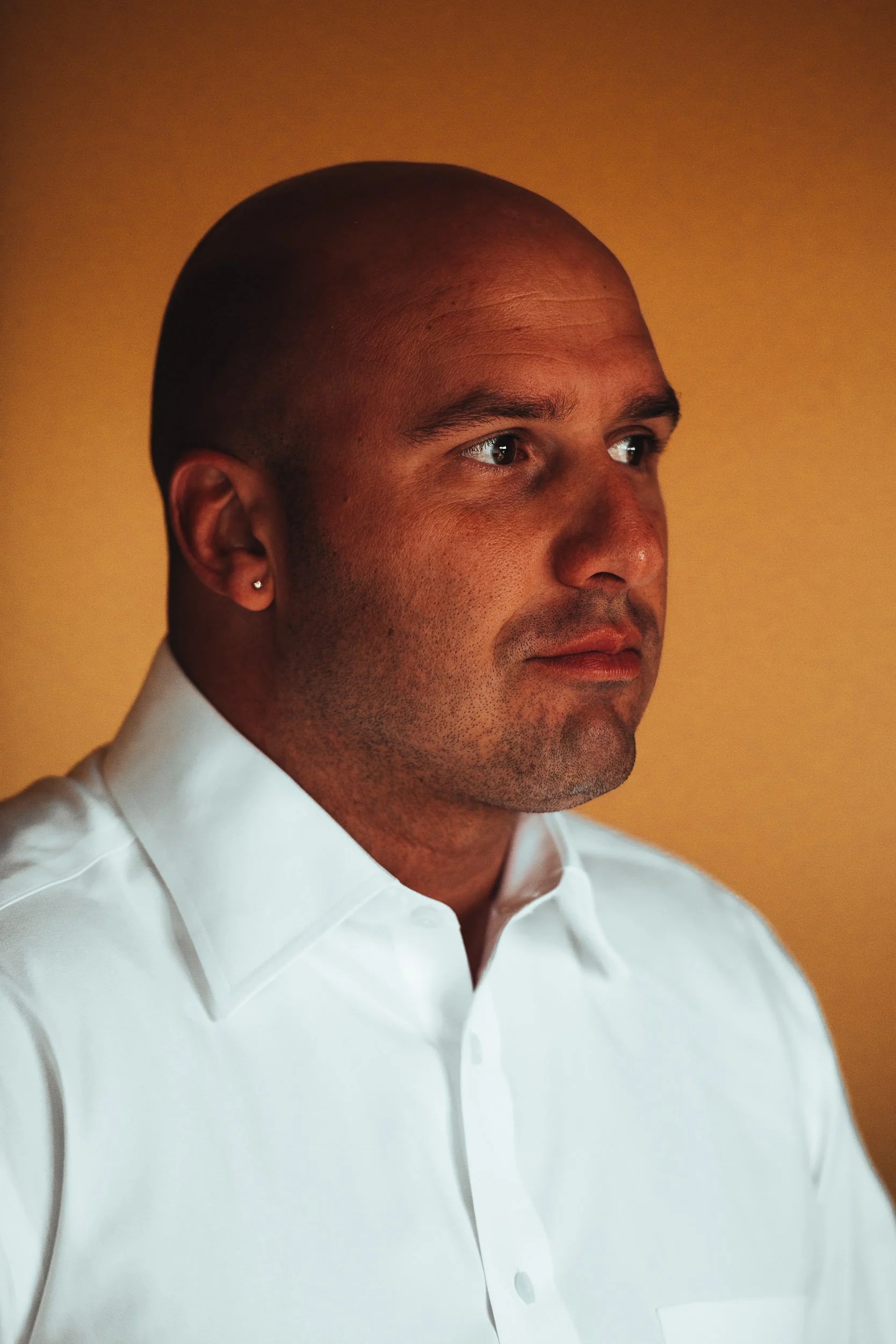 Bald man wearing a white dress shirt against a yellow background.