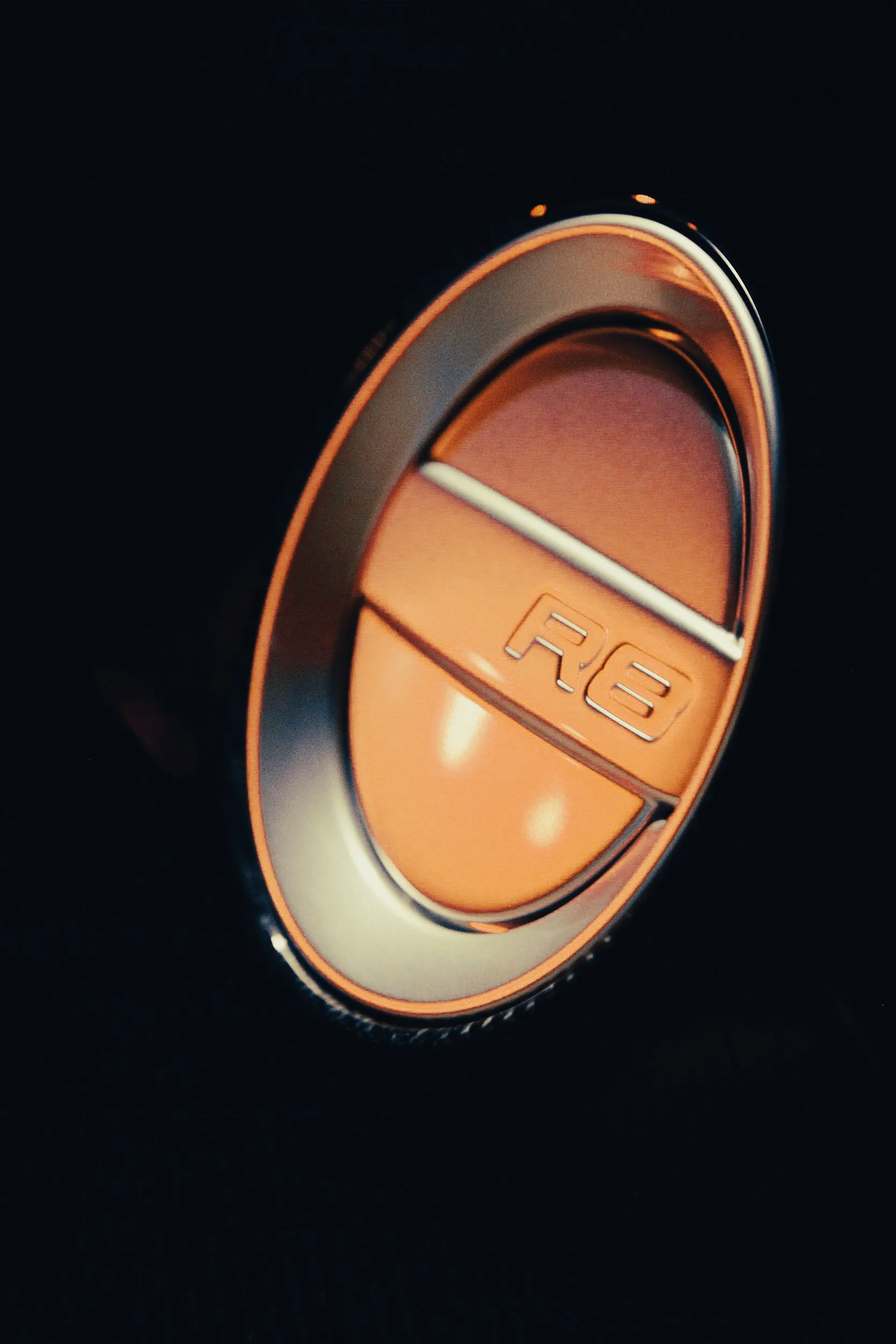 Close-up of an orange and silver car fuel cap with 'R8' embossed on it.