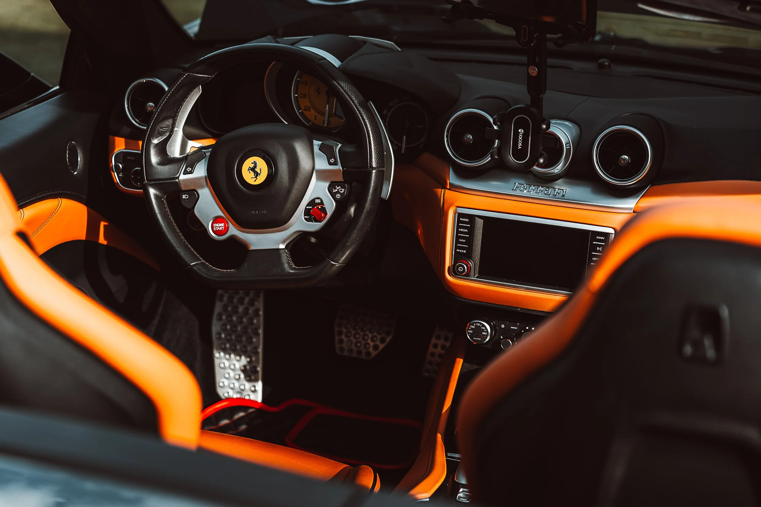 Interior of a luxury sports car featuring a steering wheel with branded emblem, leather upholstery, control buttons, and modern dashboard elements.