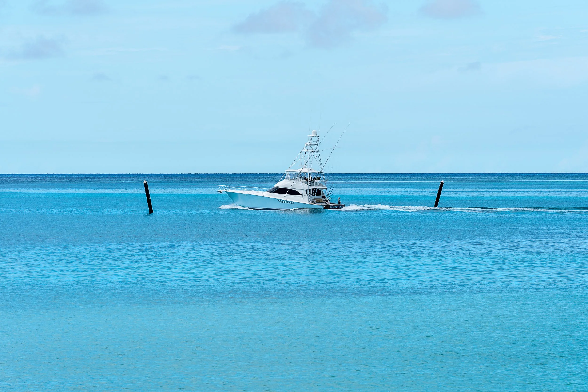 A motorboat traveling in clear blue ocean waters under a partly cloudy sky with two marker posts in view.