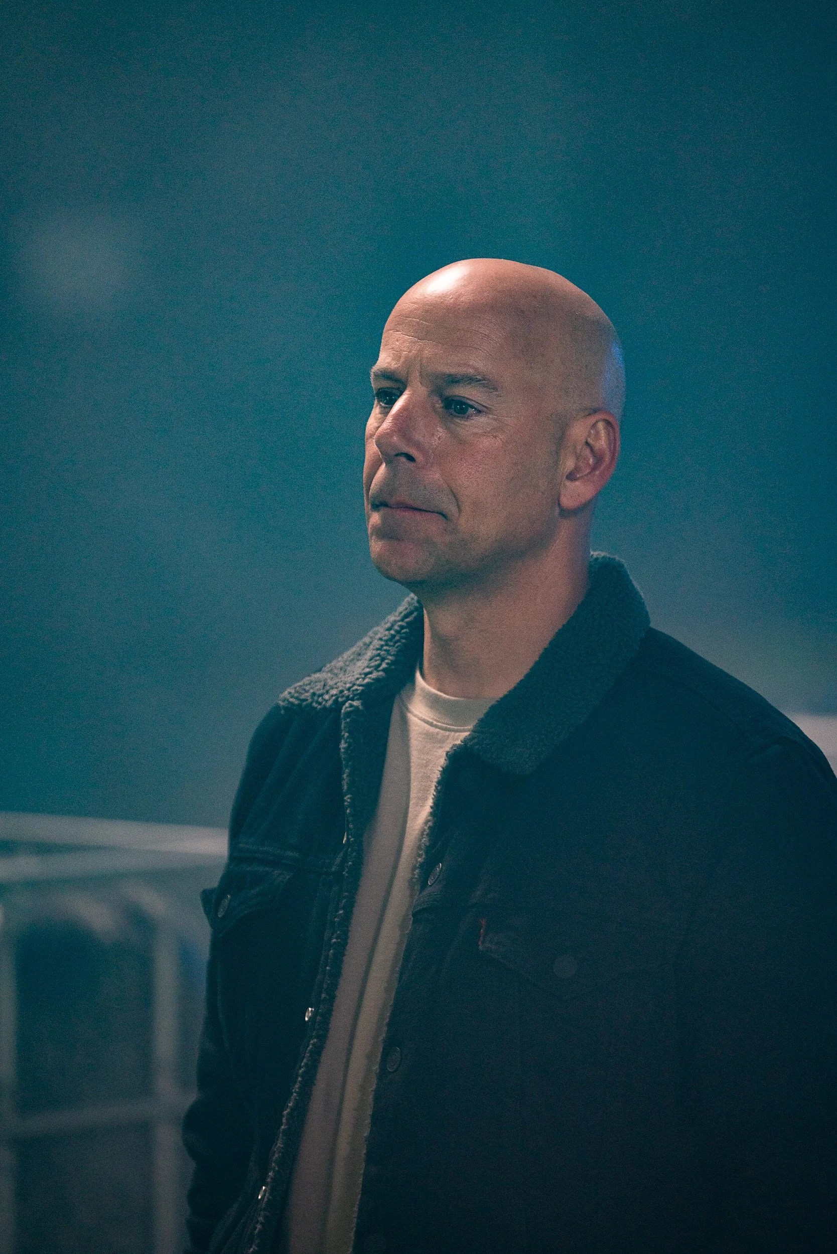 Bald man in a dark jacket with a fuzzy collar indoors