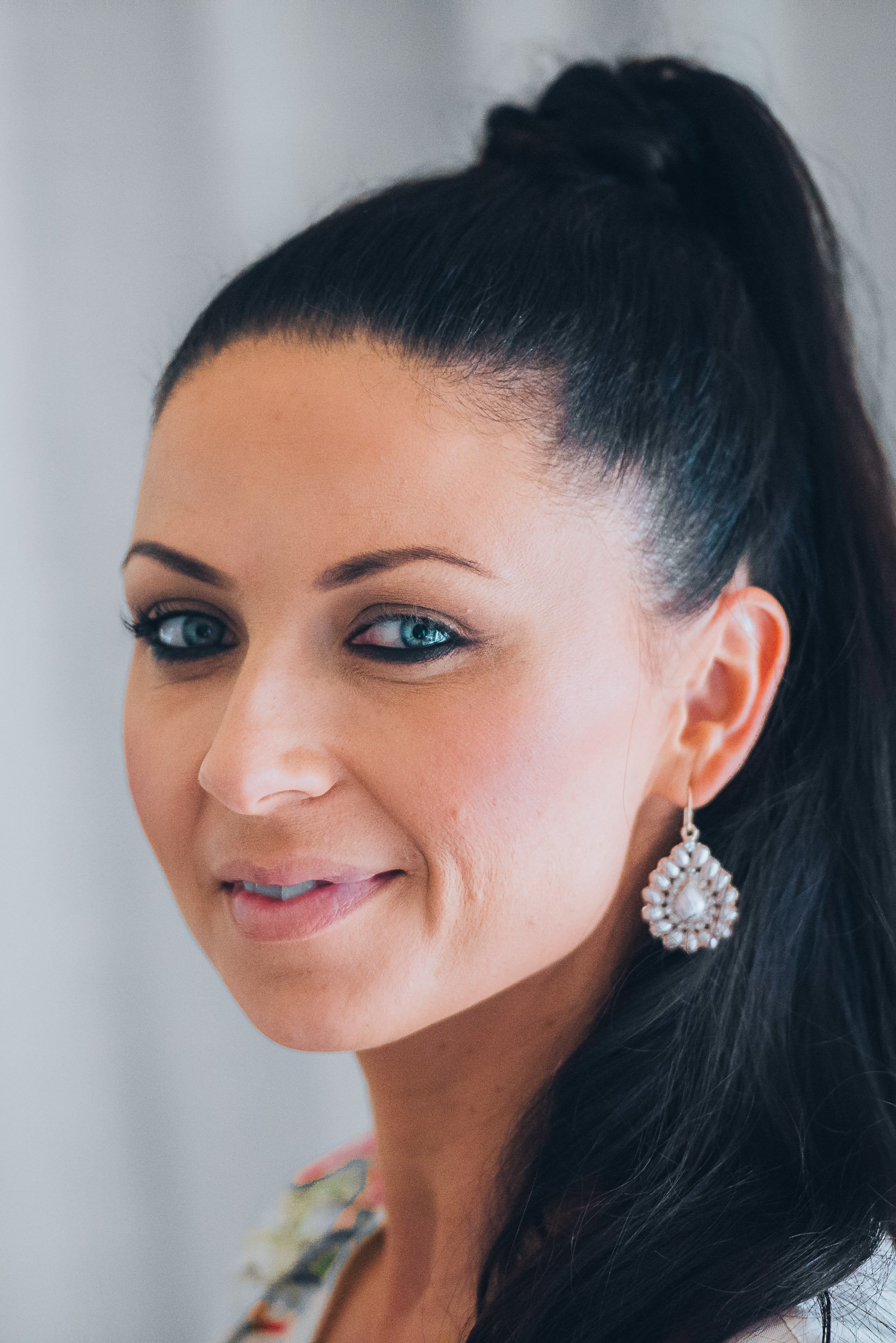 Woman with dark hair and pearl earrings smiling slightly