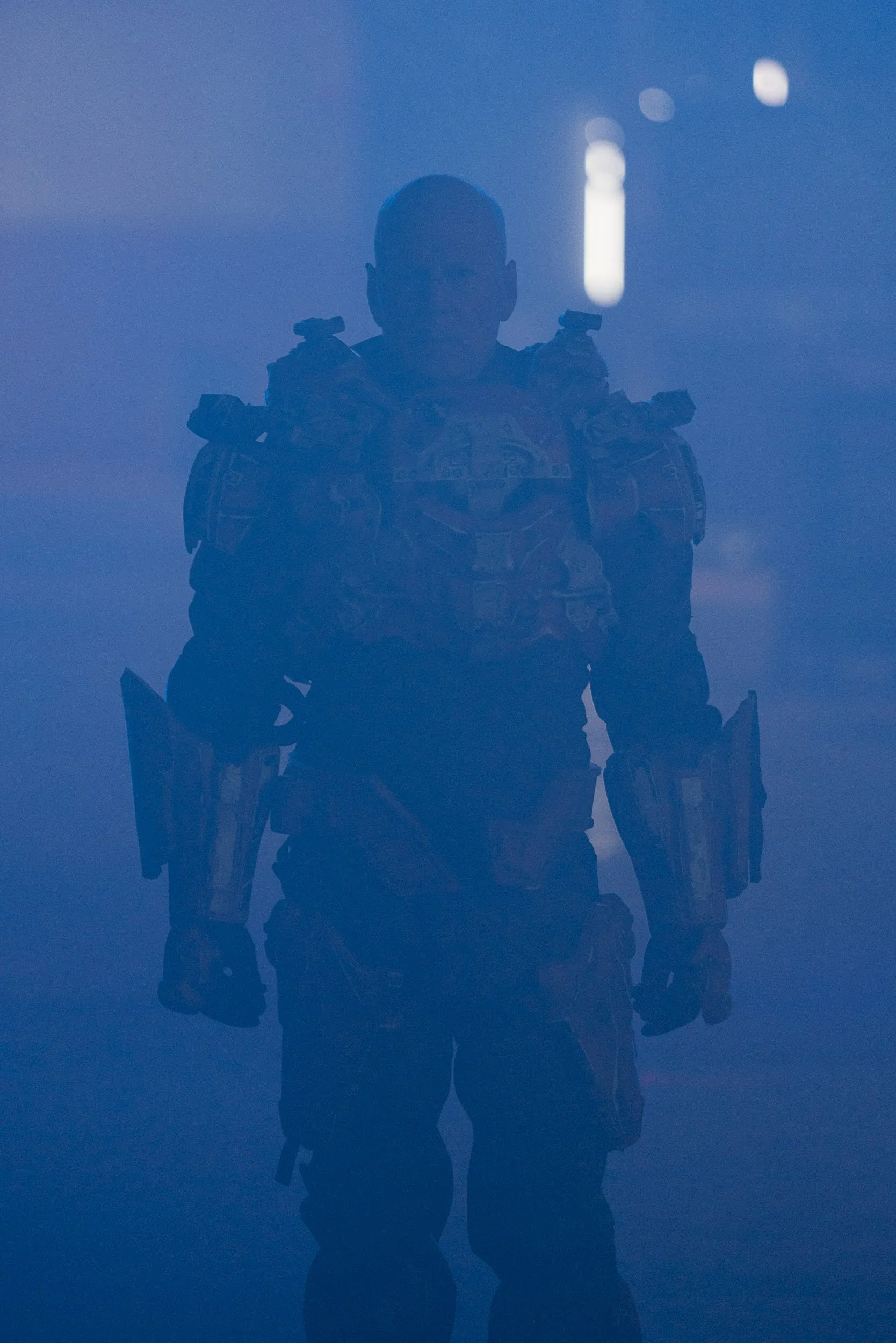 Silhouetted figure in armored suit standing in a blue-hued, foggy environment.