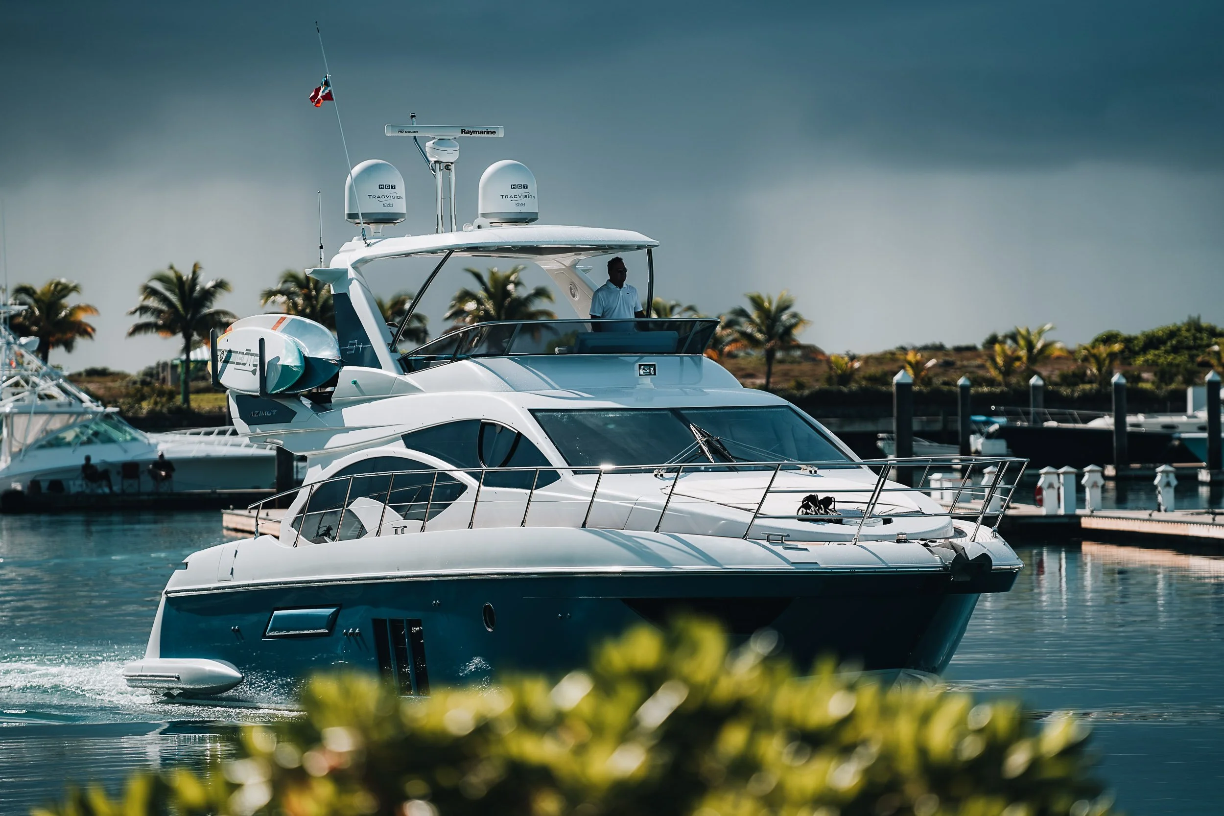 Luxury yacht cruising in a marina with palm trees in the background.