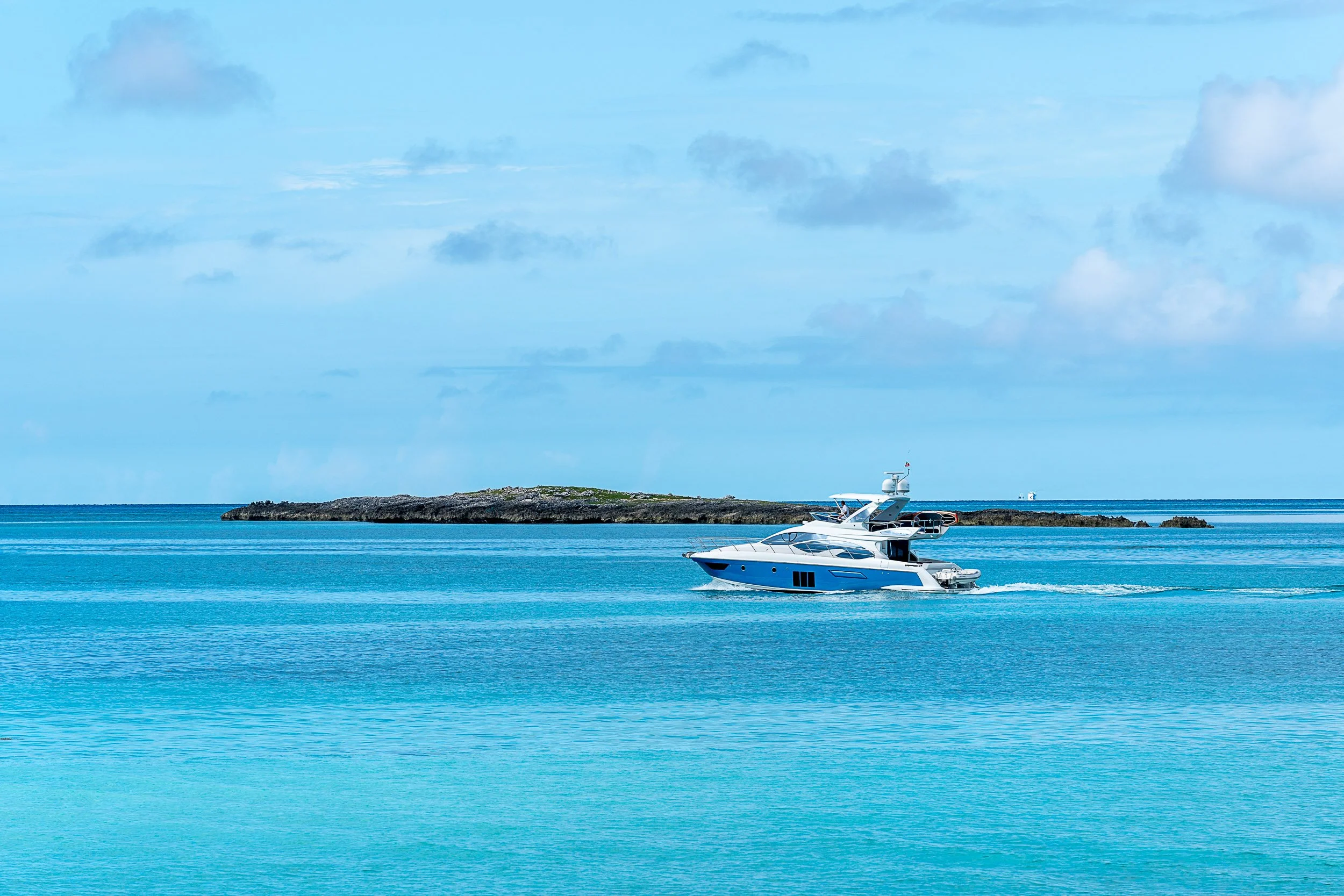 Luxury yacht on clear blue ocean near rocky island under blue sky.