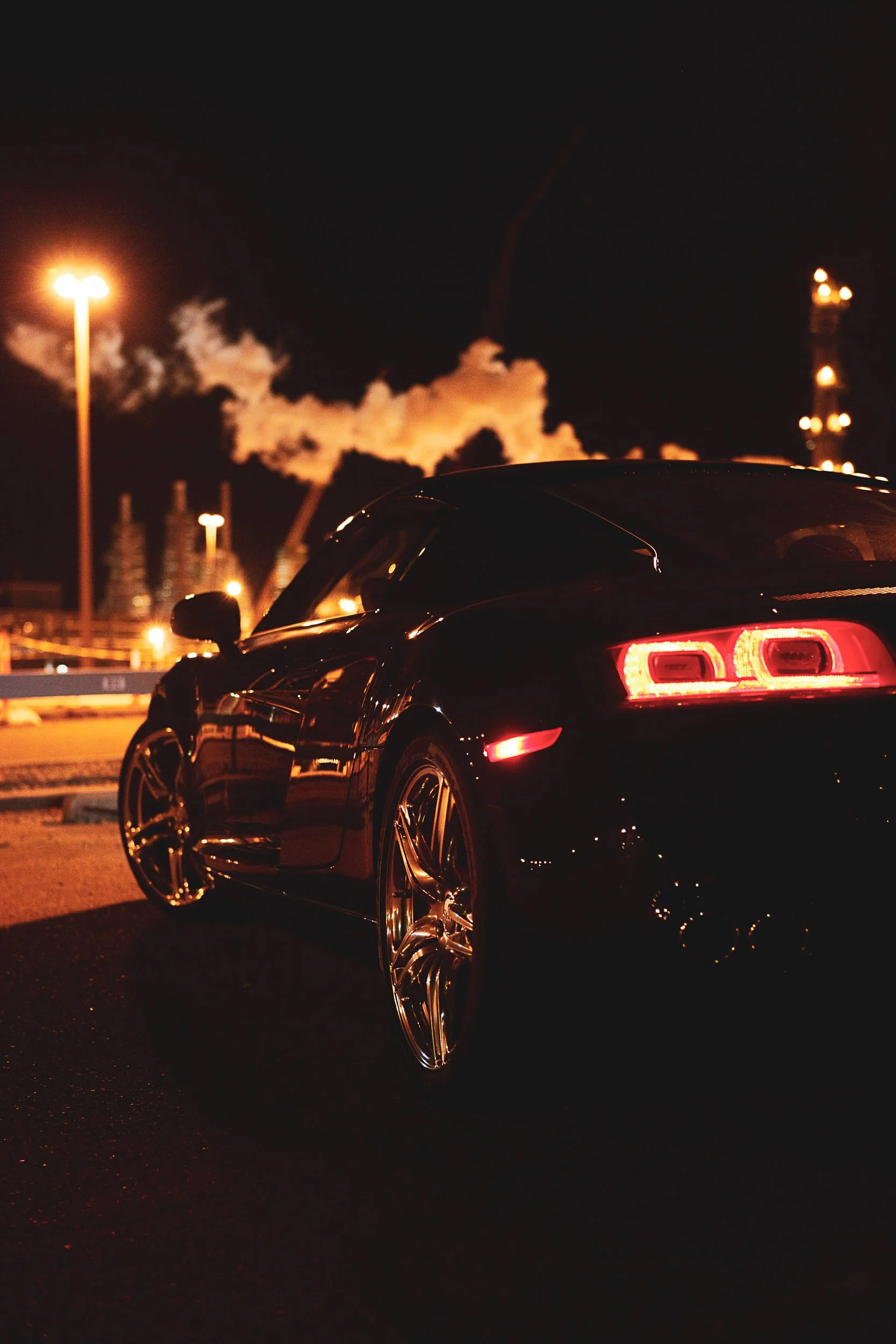 Luxury sports car with illuminated taillights at night, industrial background with smoke