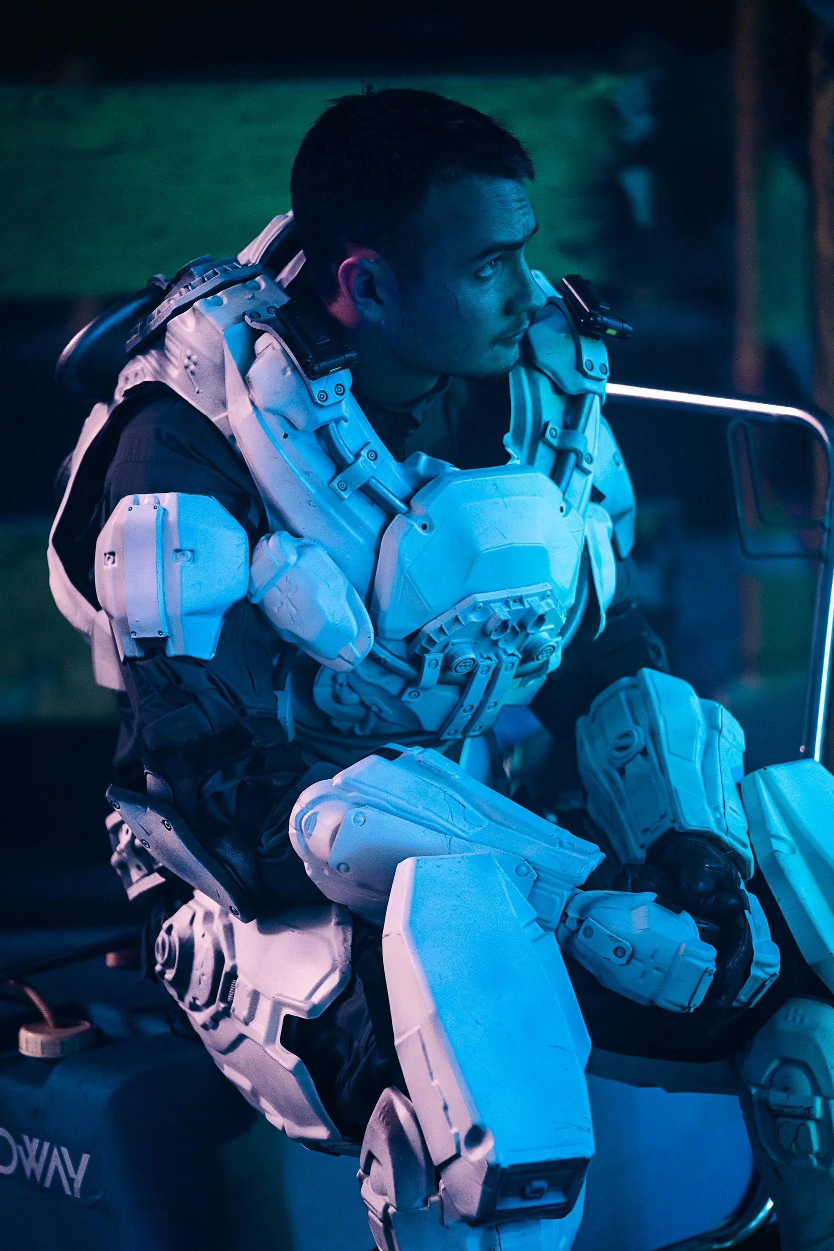 Person wearing futuristic armor, sitting in a dimly lit environment with a blue hue.