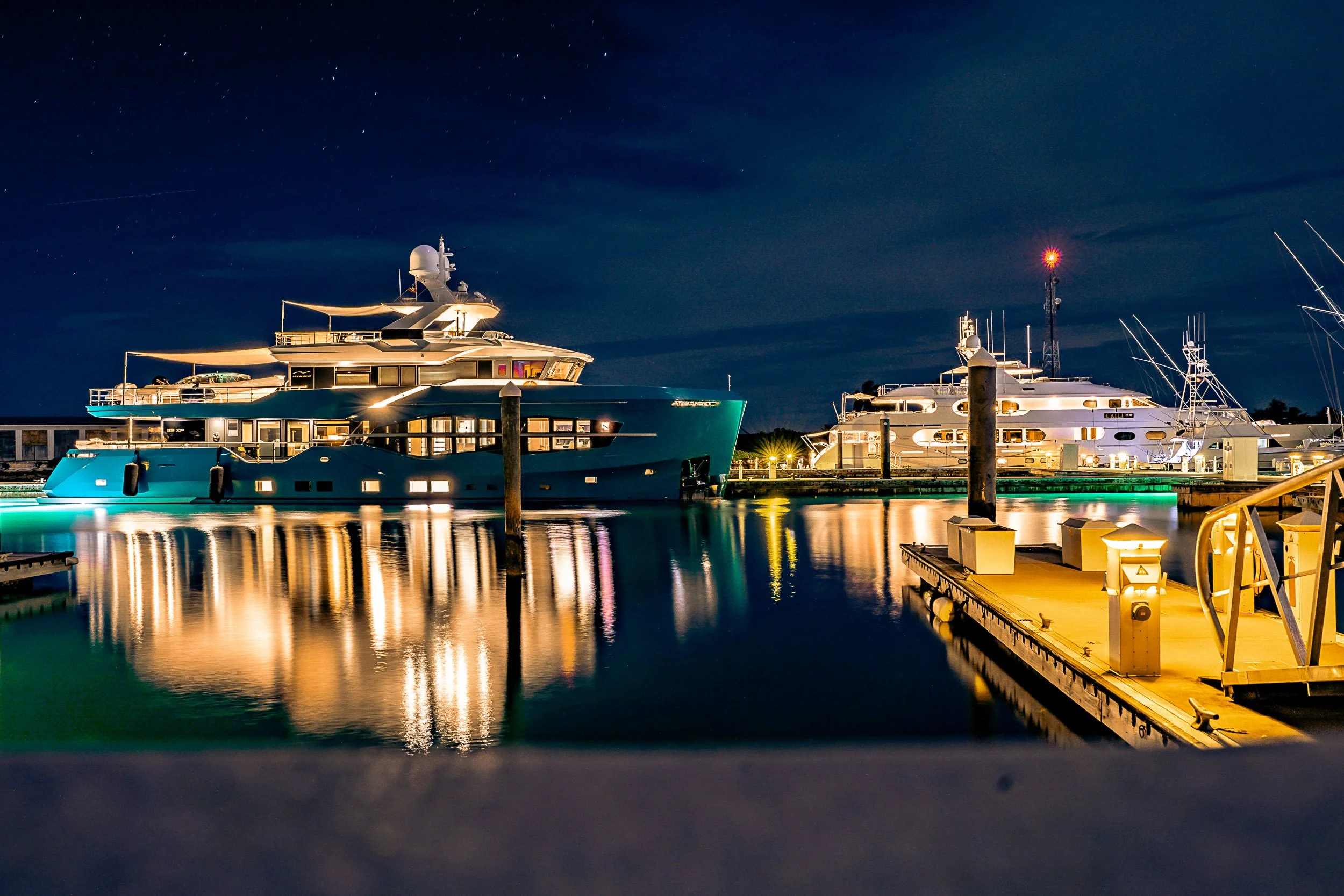 Luxury yachts illuminated at night in a marina with reflections on the water.