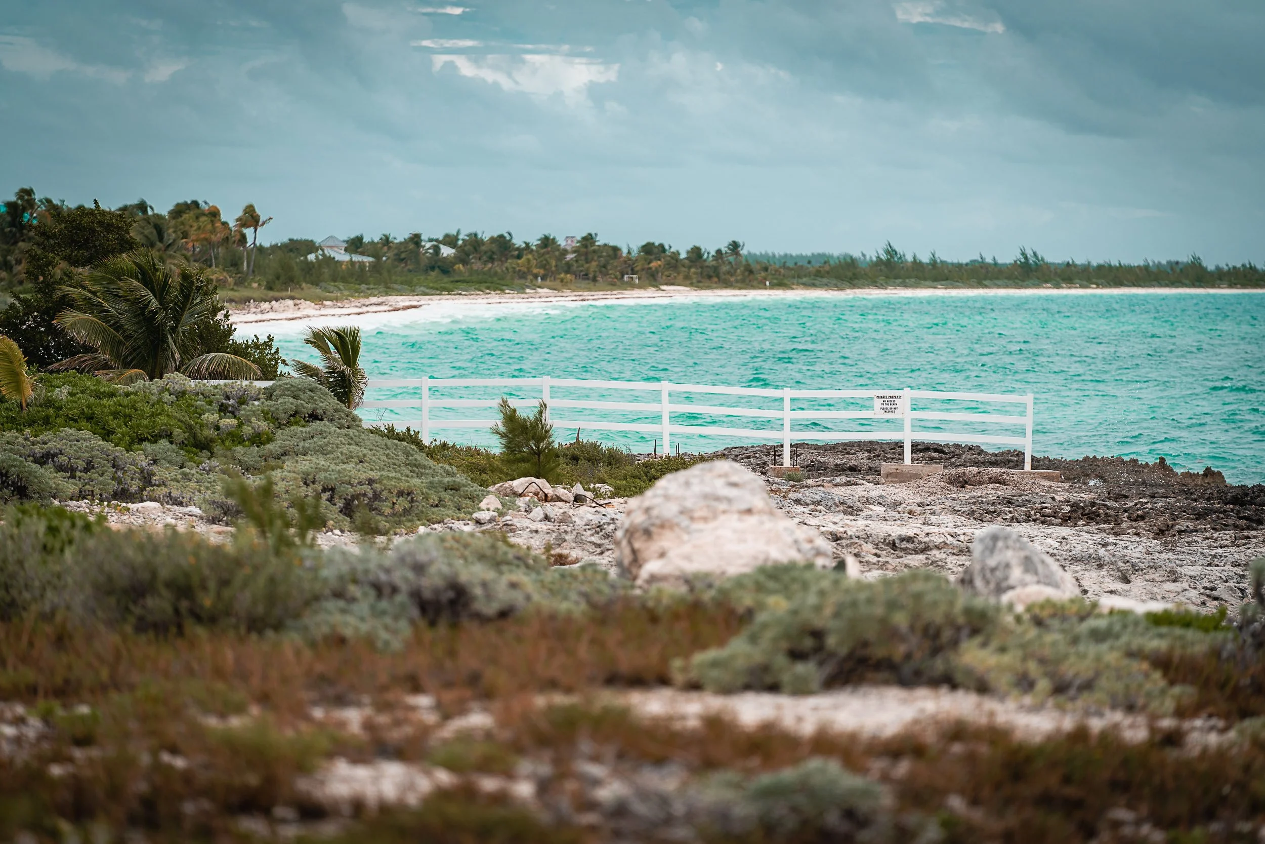 Tropical beach with turquoise water, rocky shore, and white fence.